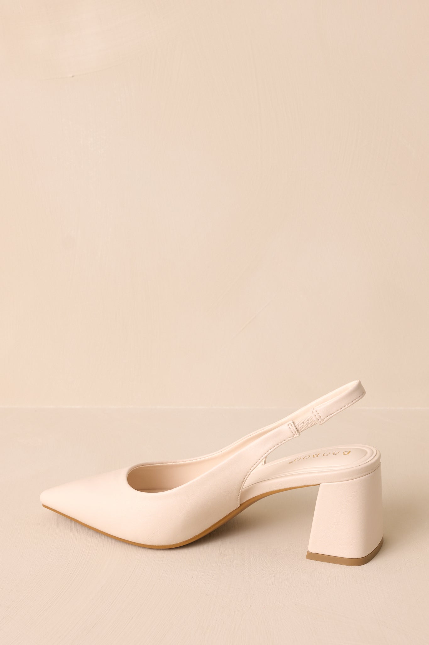 A side perspective of the ivory heels, emphasizing the pointed toe, smooth faux leather material, and thick block heel with the back strap clearly visible.