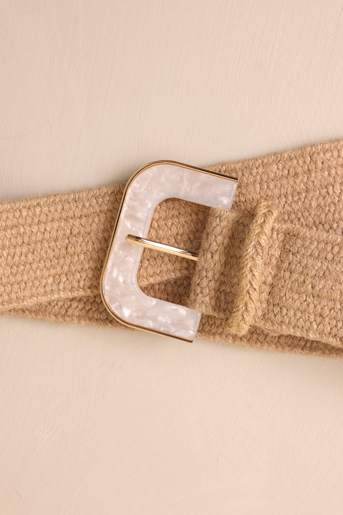 A full shot of the tan woven belt laid flat against a beige surface, showcasing its design and materials.