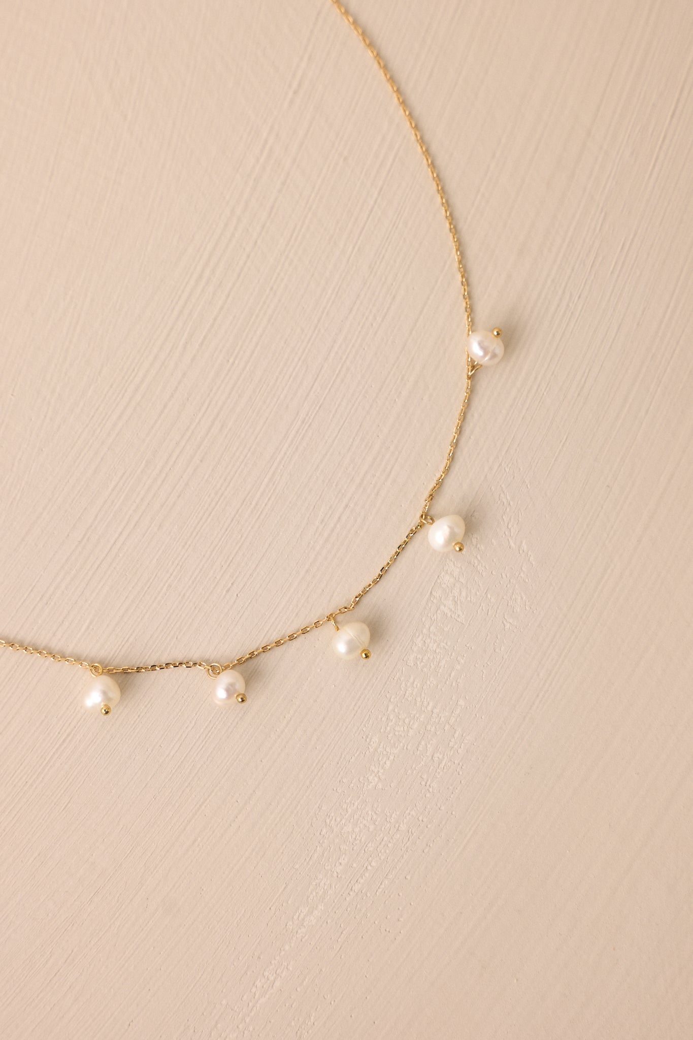 Extreme close-up of the gold necklace, highlighting the delicate thin chain and the seven small ivory faux pearls with a lobster claw clasp.