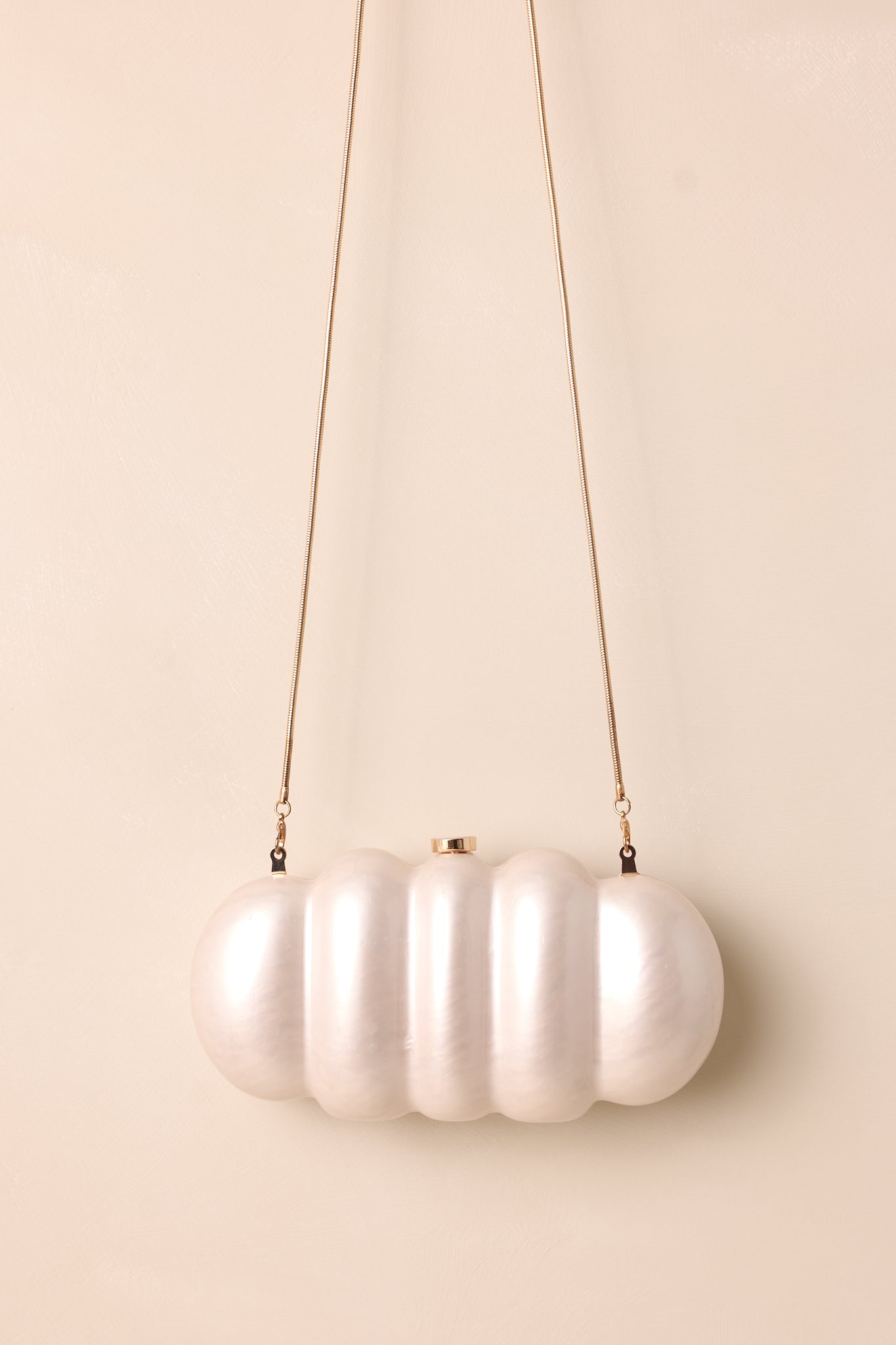 Ivory clutch angled to showcase both the gold chain and pearlescent texture against a neutral backdrop.