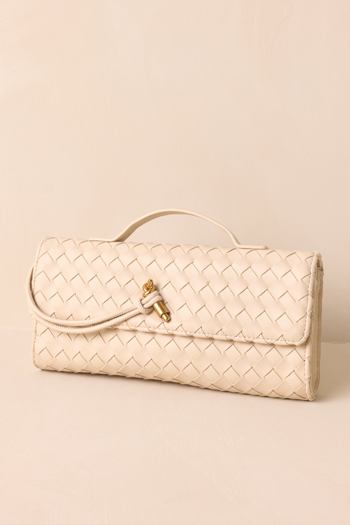 A front-angled view of the ivory handbag, highlighting its structured rectangular shape, gold hardware, and magnetic flap closure.