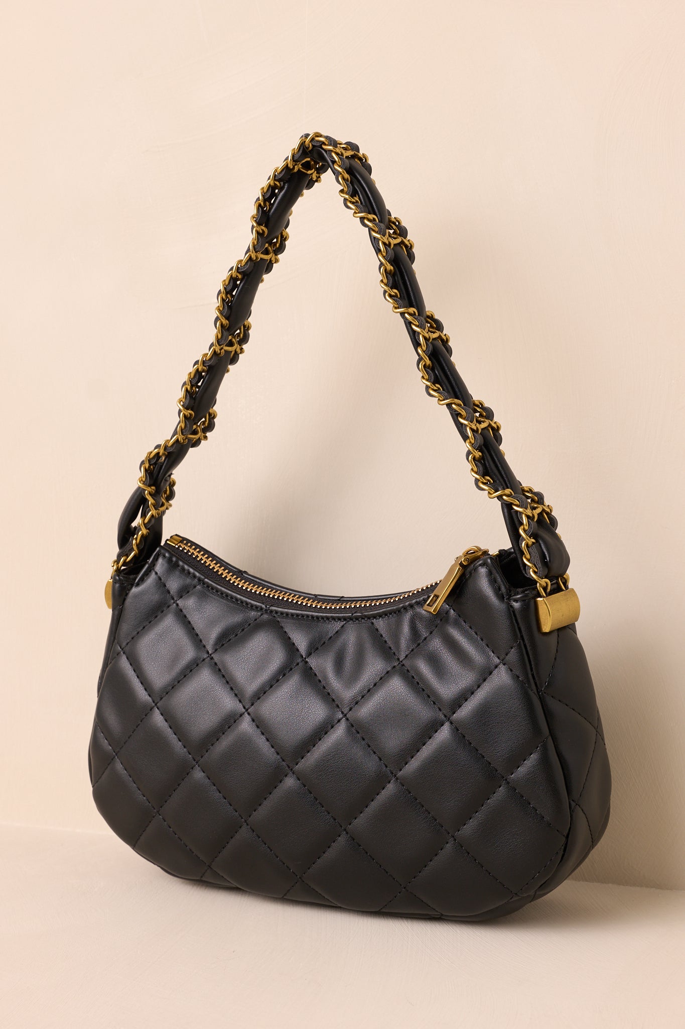 Black handbag highlighting the gold zipper closure and sleek faux leather material.