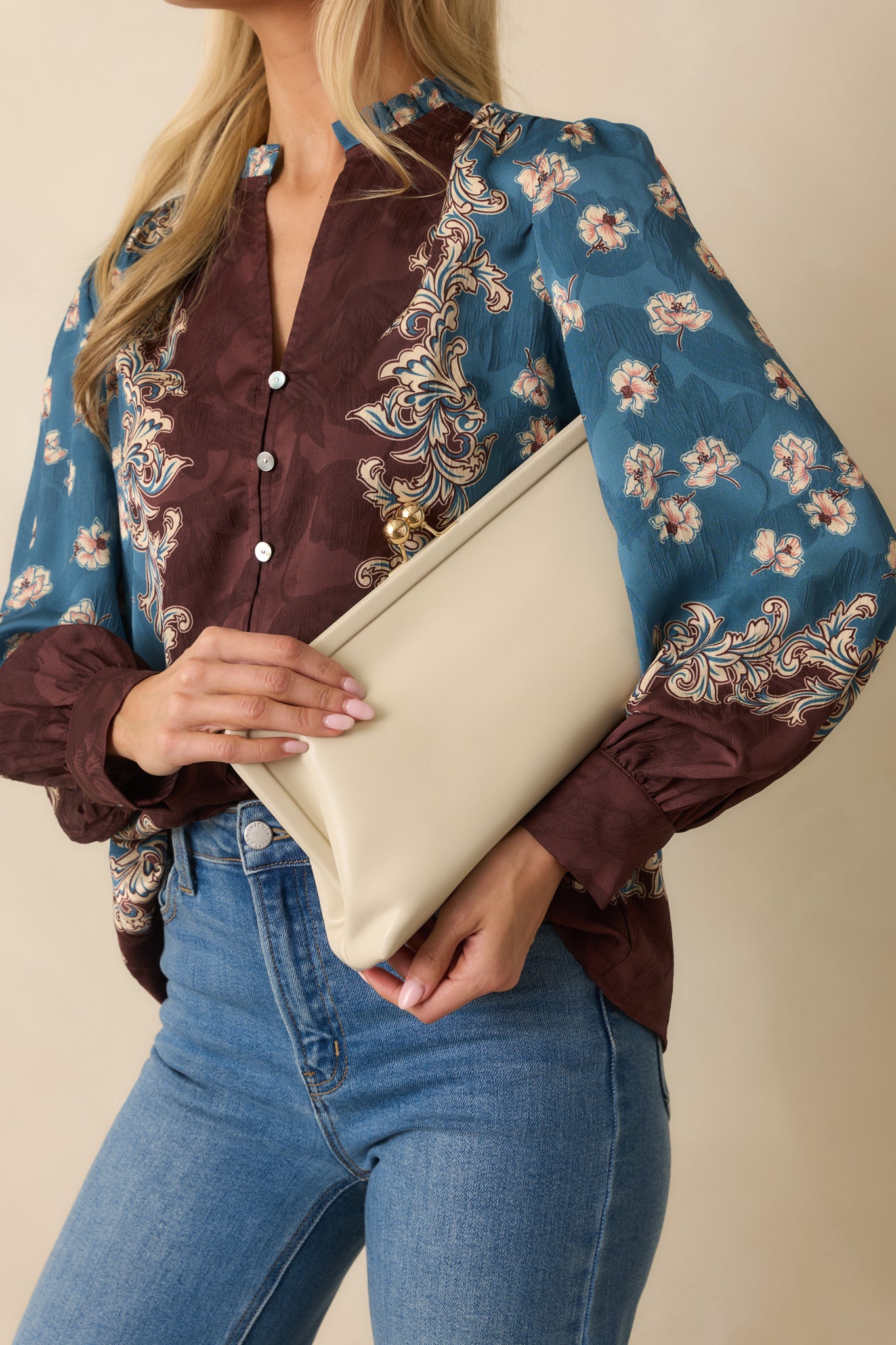 An angled detail of the ivory clutch featuring a kiss-lock closure, smooth faux leather finish, and lined interior.