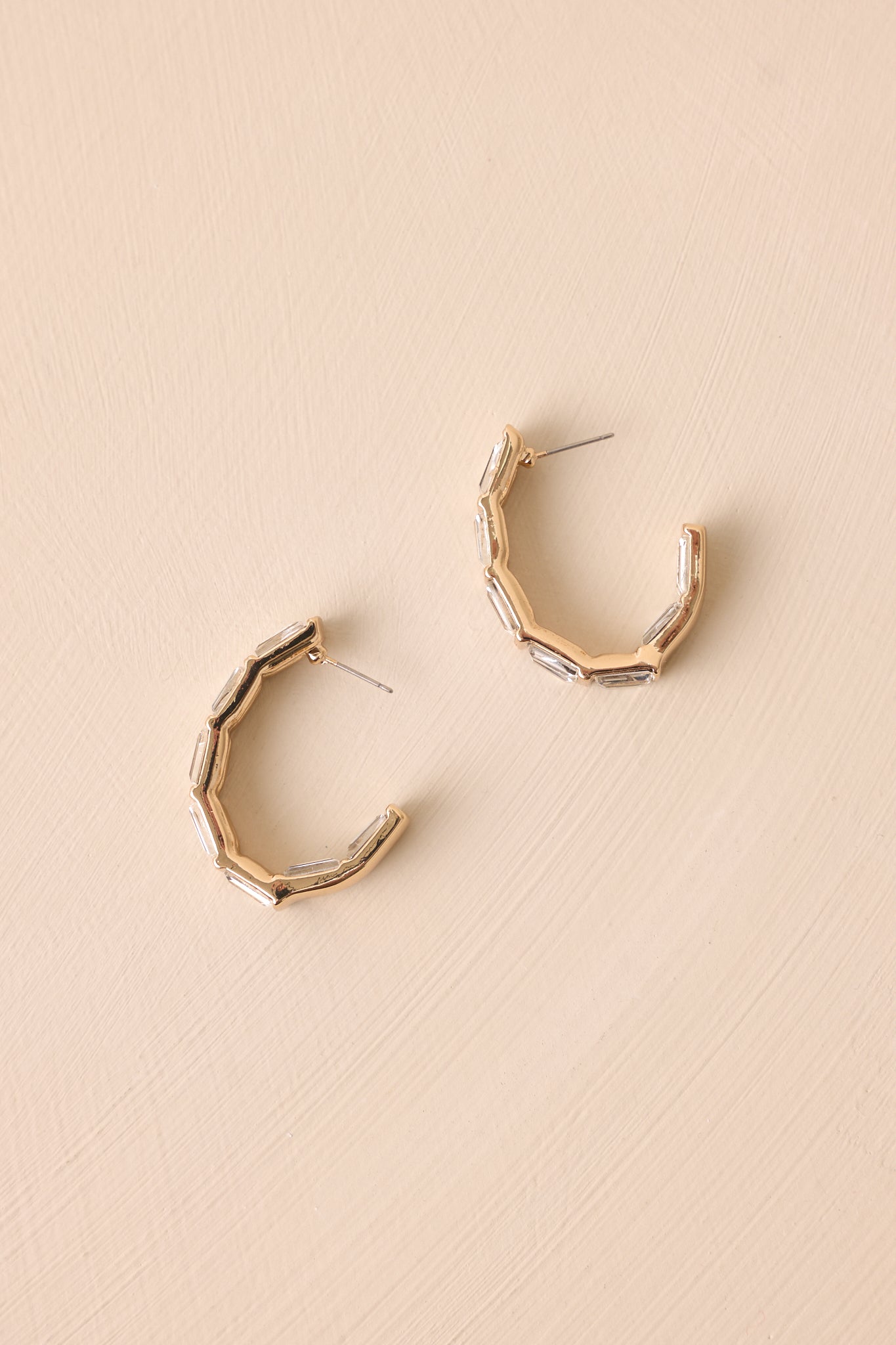 A slightly different angle of the earrings on a beige backdrop, emphasizing the gold hardware and secure back postings.