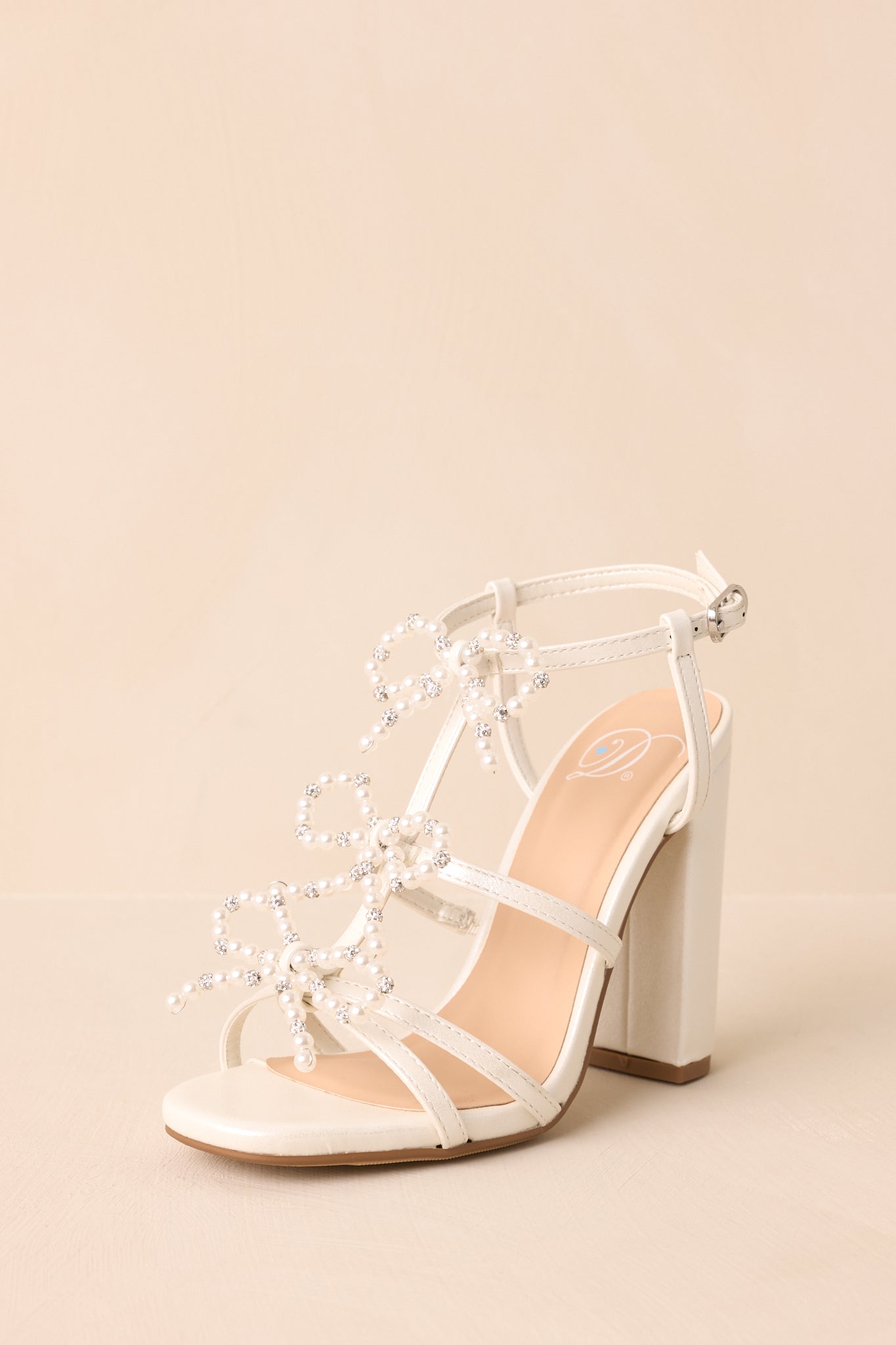 An angled front view capturing the sparkle of the ivory finish and the bow details aligned down the toe strap.