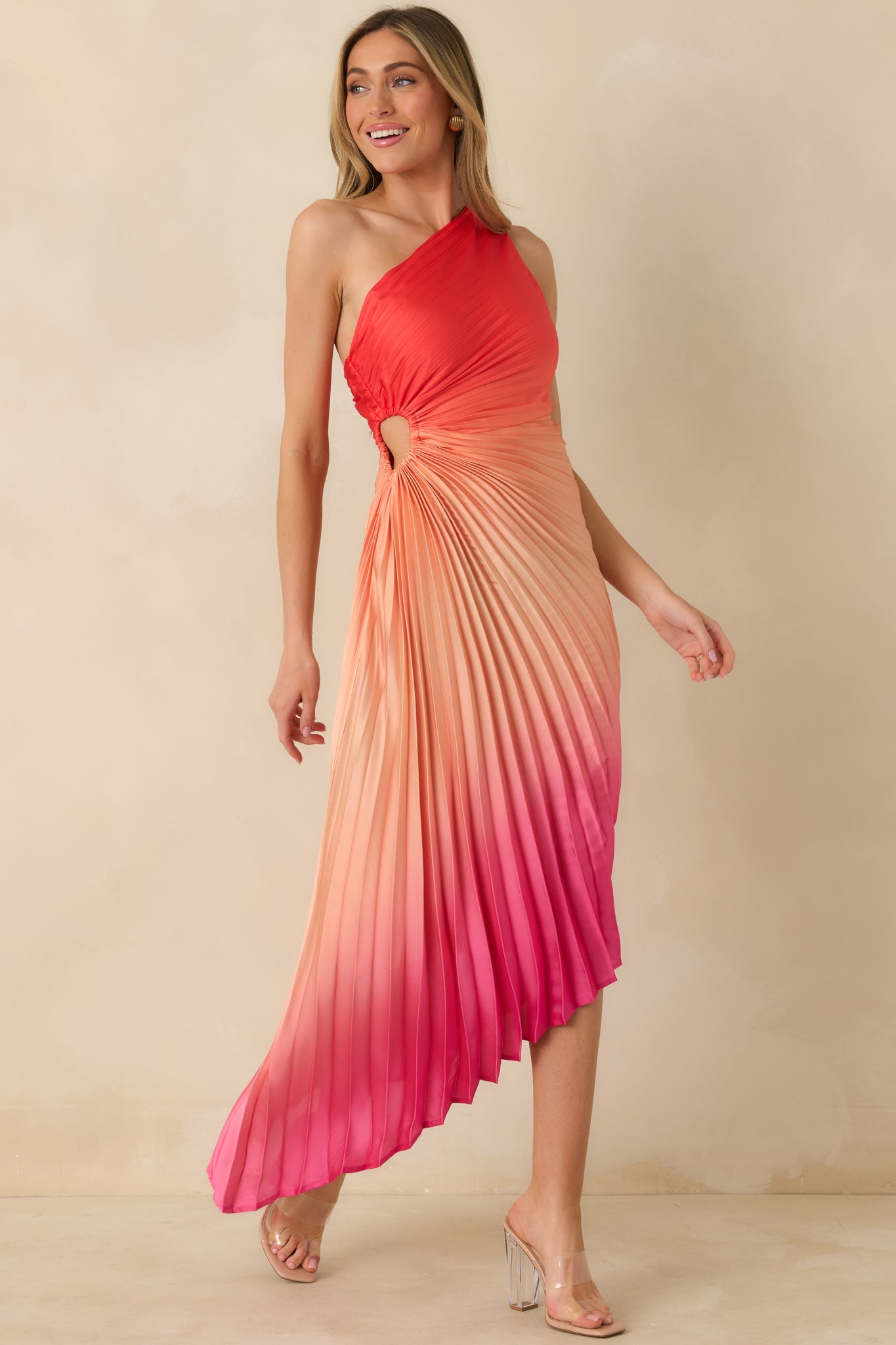 Angled front perspective highlighting the pleated detailing, small side cutout, and asymmetric hemline of the coral maxi dress.