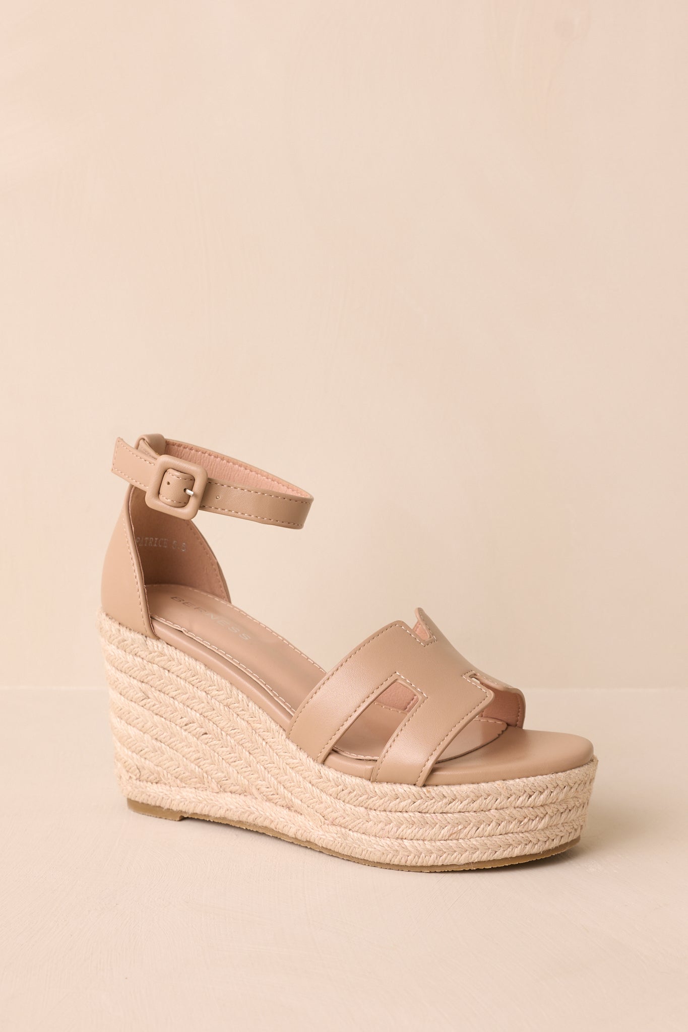 A slightly angled shot emphasizing the beige woven straw platform wedge heel and how it connects to the tan ankle strap.