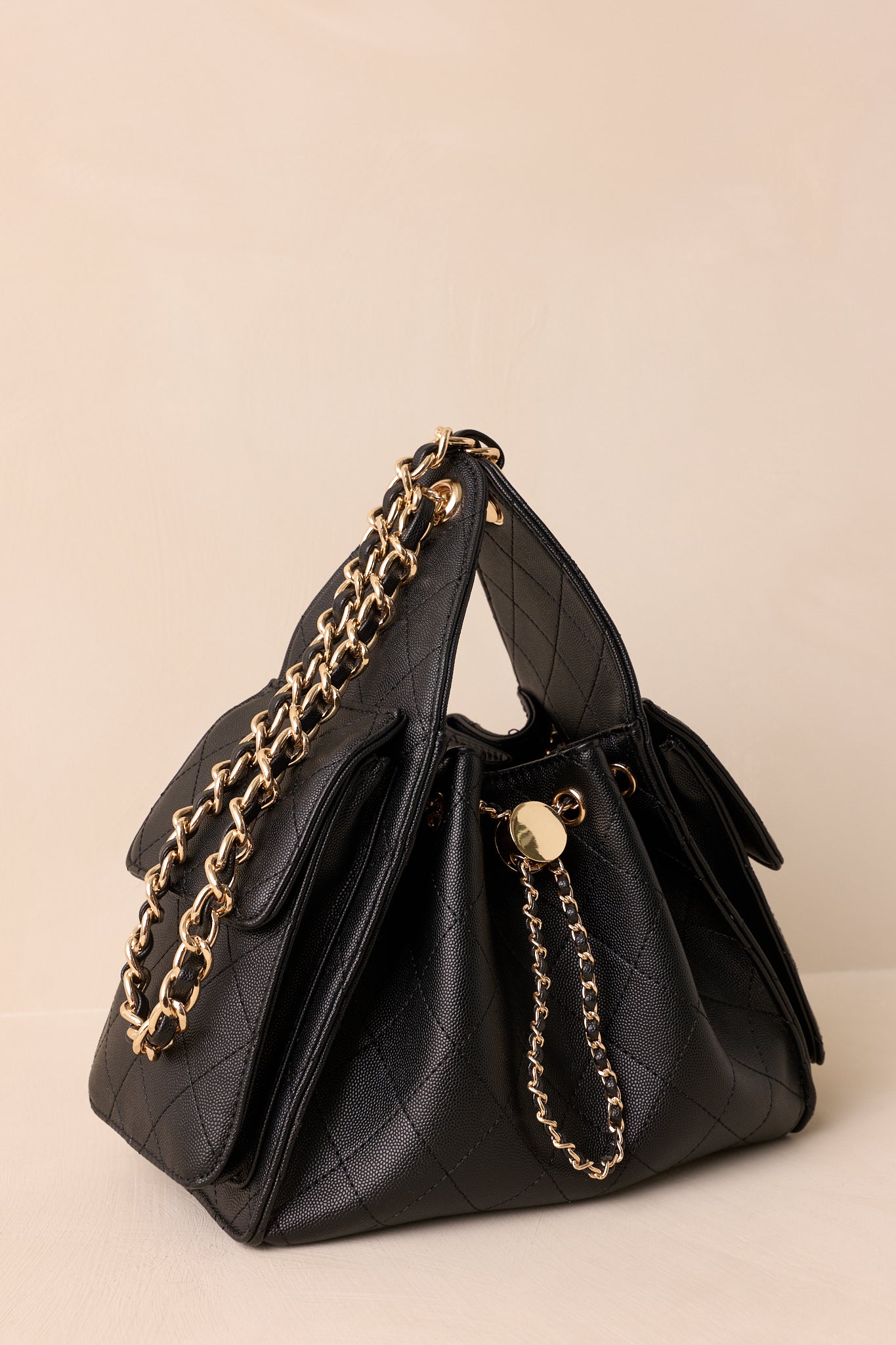 Angled view of the black quilted purse showing the gold and faux leather drawstring and large side pockets with fold-over flaps.