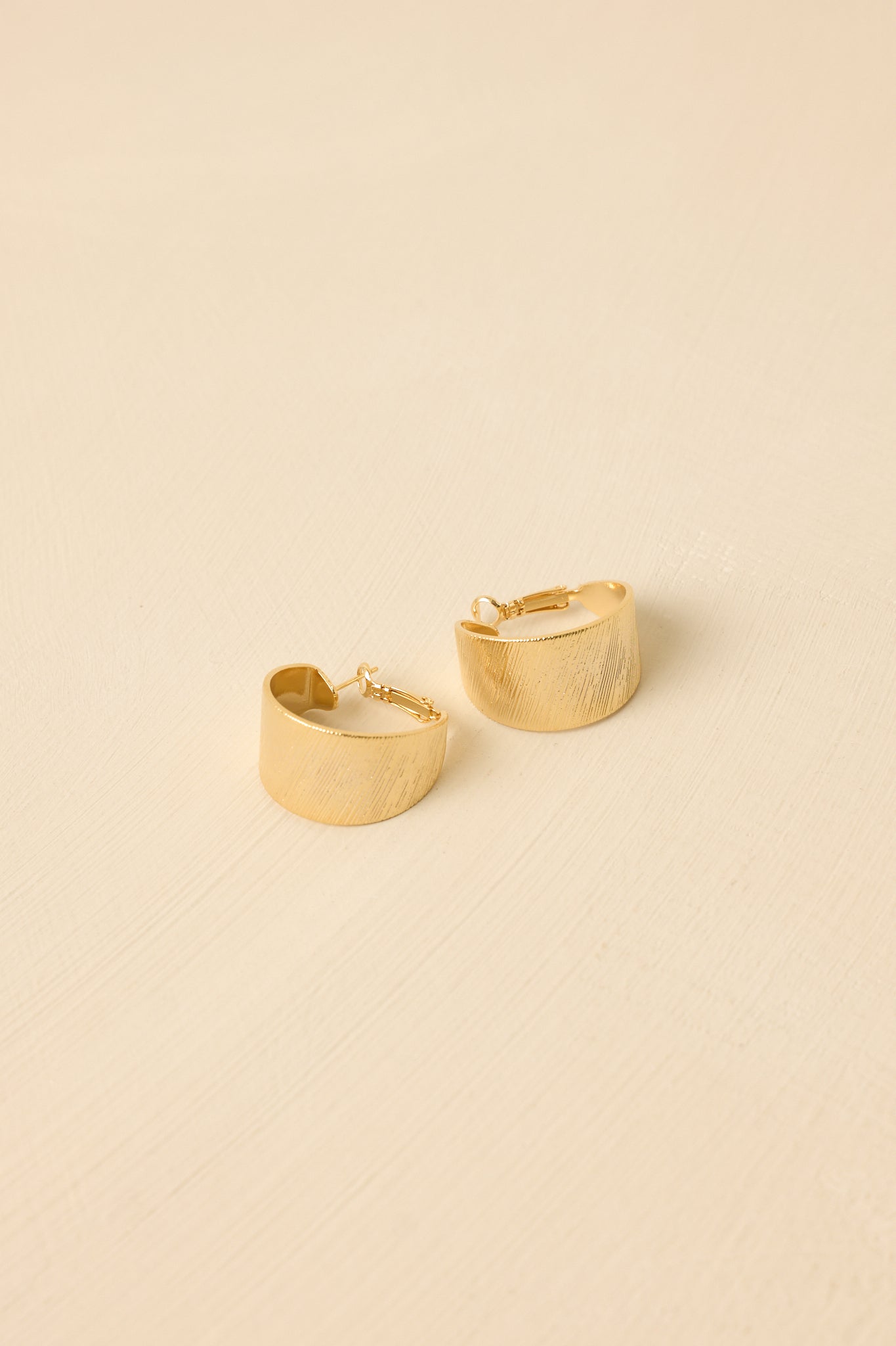 Angled view of the earrings against a beige backdrop highlighting the wide silhouette and secure hinged closure.