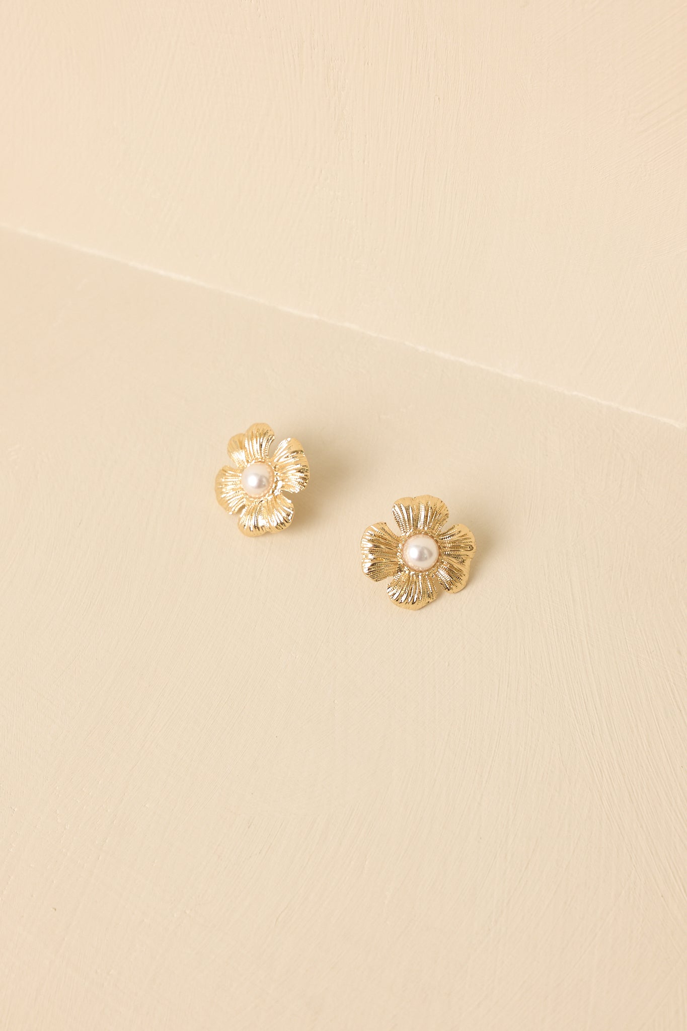 Angled view of the earrings against a beige backdrop highlighting the sculpted floral design and polished gold-tone finish.