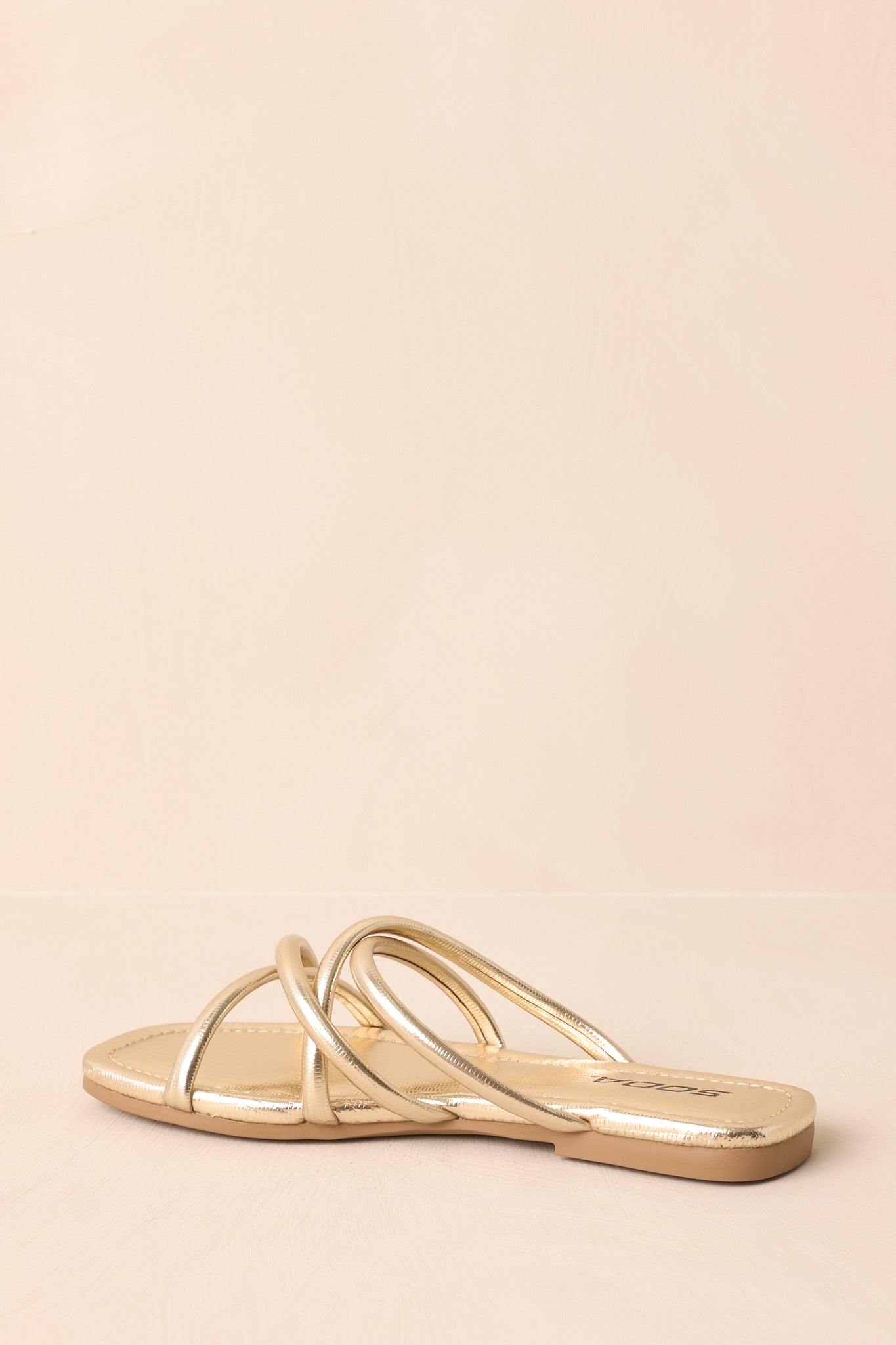An angled view focusing on the back and side design of the metallic sandal, showing the heel section of the tan rubber sole.