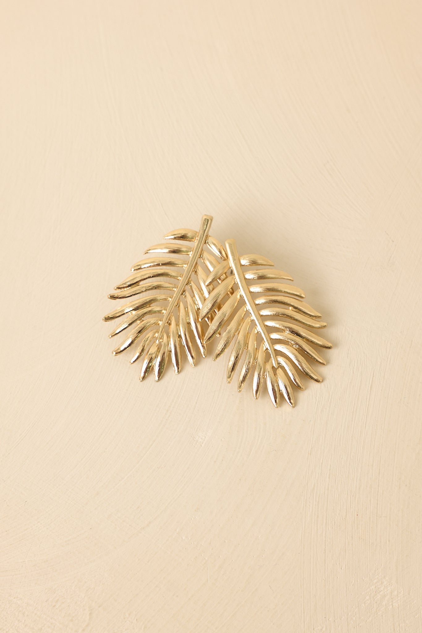 Angled view of leaf-inspired drop earrings on beige backdrop highlighting polished finish and dimension.