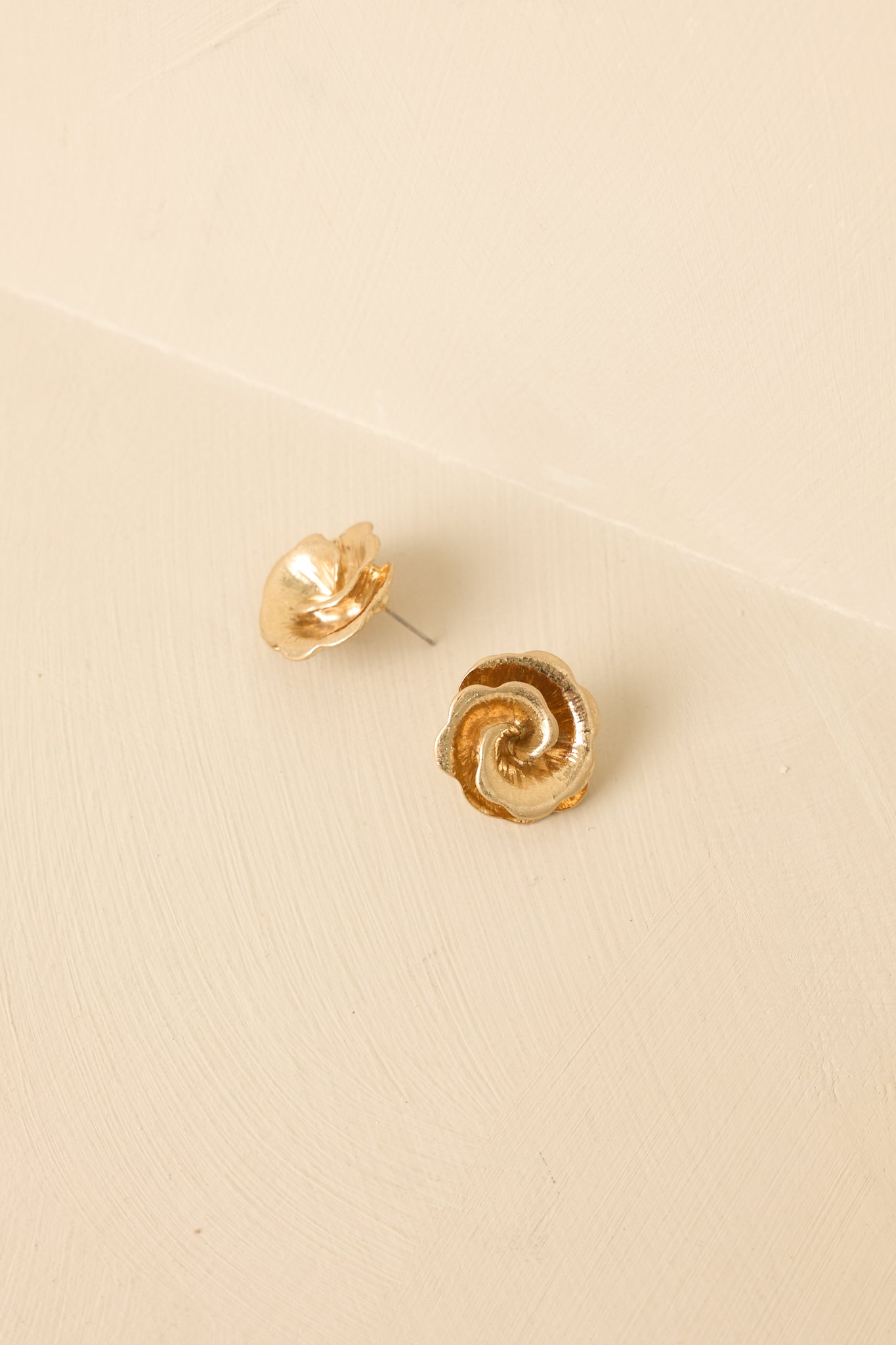 Angled view of polished gold studs on beige backdrop highlighting curved details and shine.