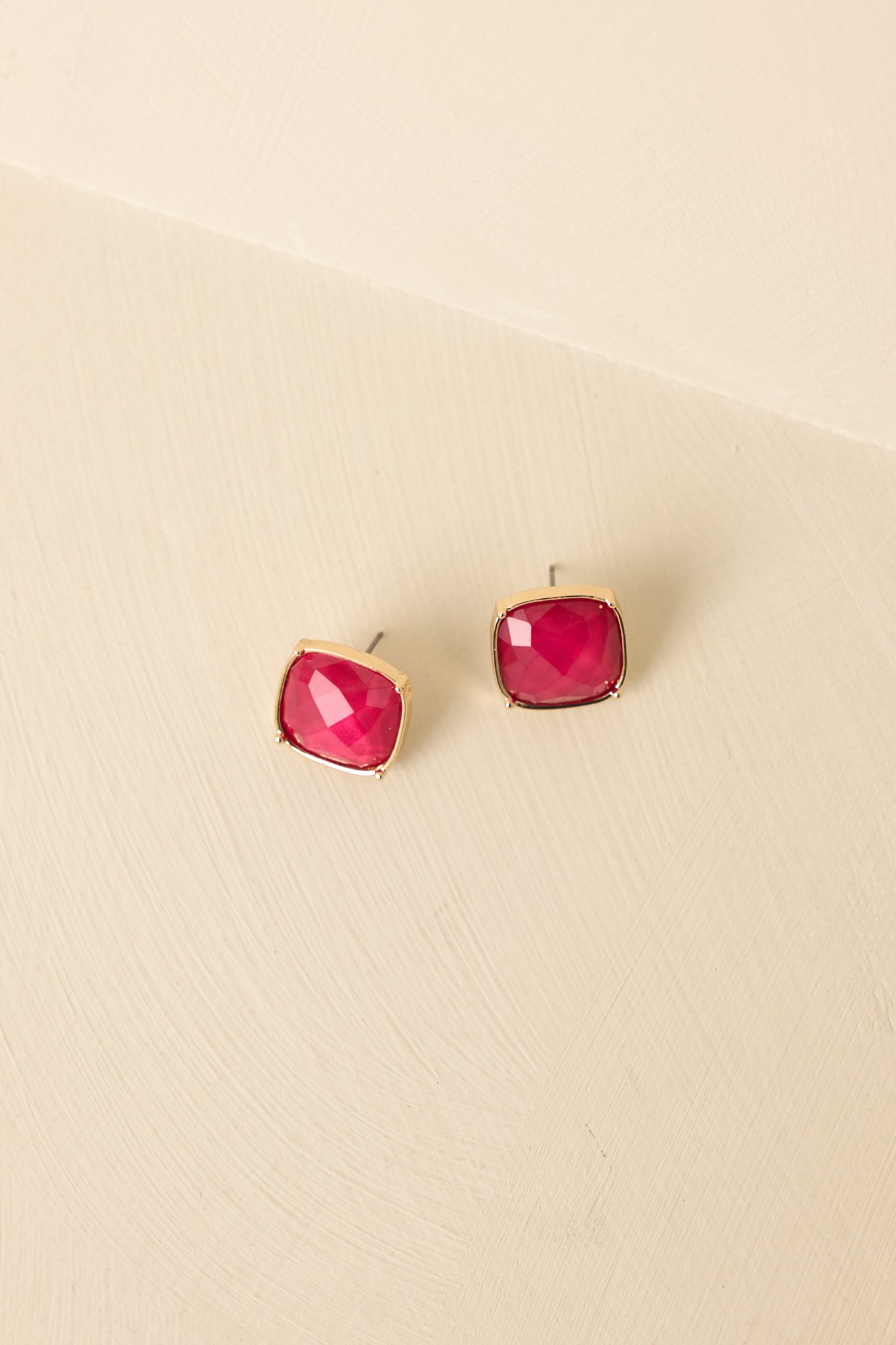 Angled view of red stone earrings on beige backdrop highlighting faceted surface and elegant finish.
