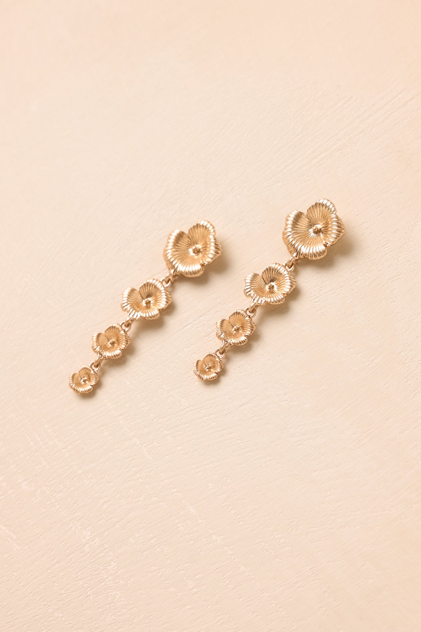 Angled view of tiered flower earrings on beige backdrop highlighting dimension and soft shine.