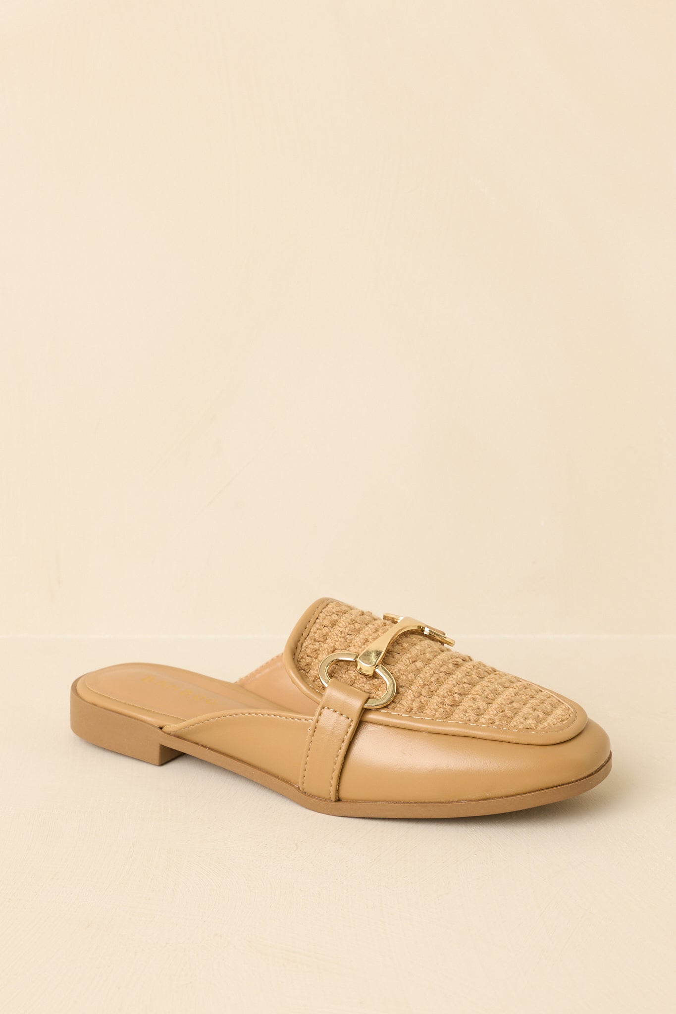 Angled view of woven faux leather loafers on beige backdrop highlighting texture and open-back style
