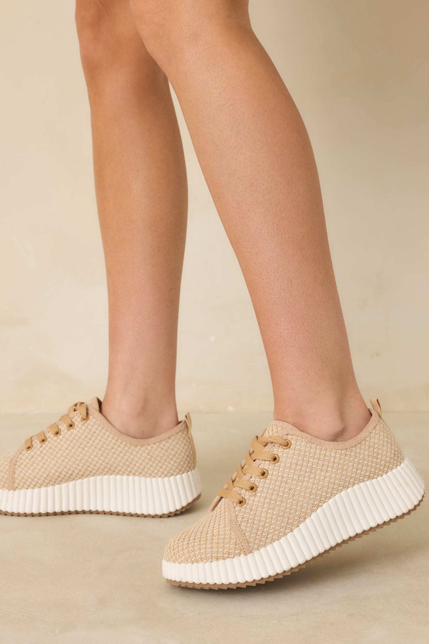 Angled view of tan woven sneakers showing the textured fabric upper and white rubber outsole.