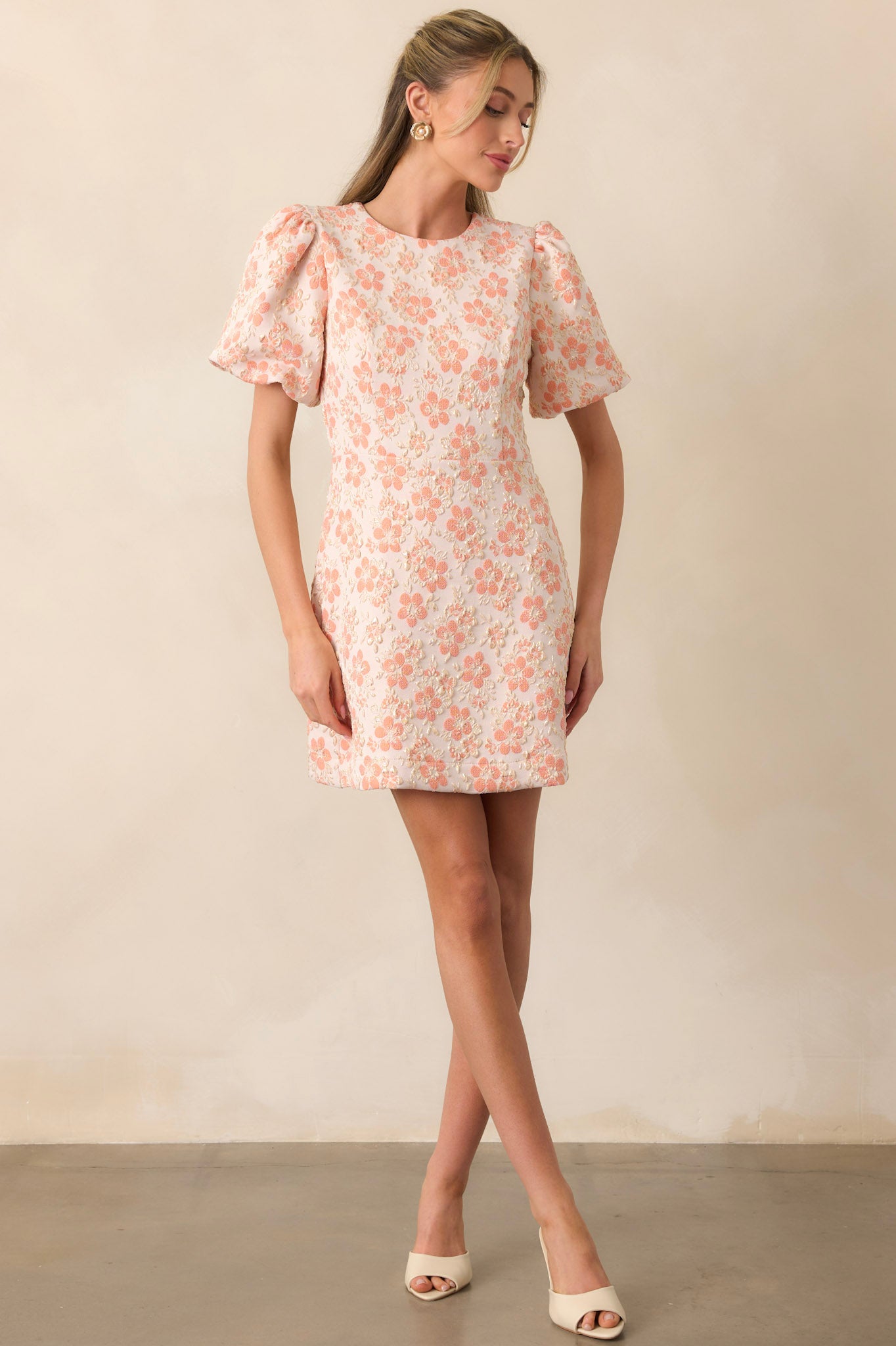 A stylish apricot mini dress with delicate gold accents, a structured fit, and puff sleeves. The subtle sheen of the fabric catches the light, highlighting the intricate details.
