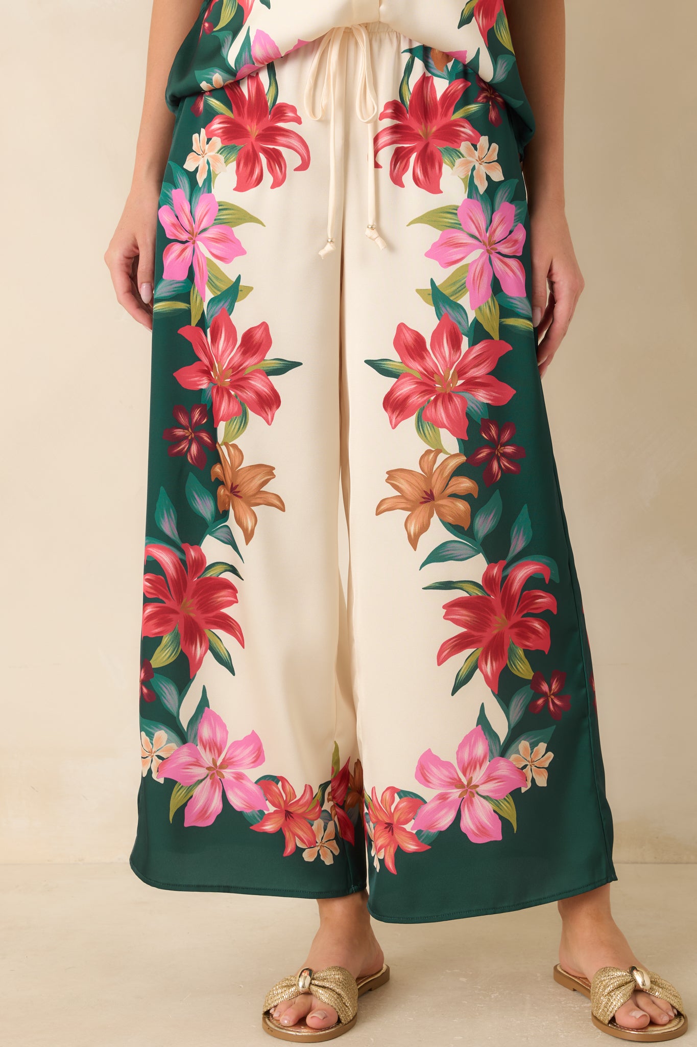 Teal satin pants showcasing the adjustable drawstring waist, lightweight fabric, and bold multi-color floral design.