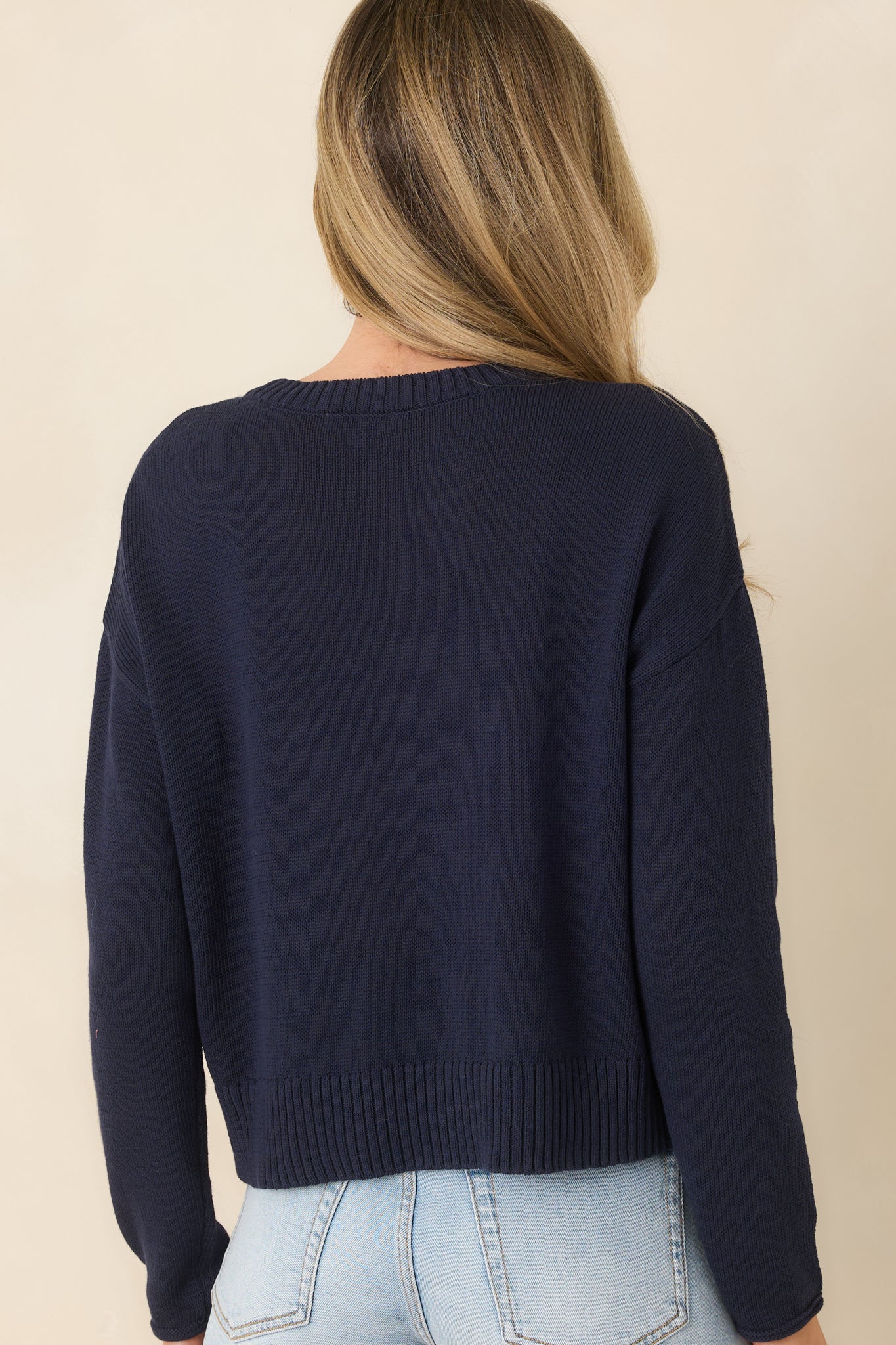 Back view of the navy blue sweater displaying long sleeves, relaxed fit, and ribbed trim at hem and cuffs.