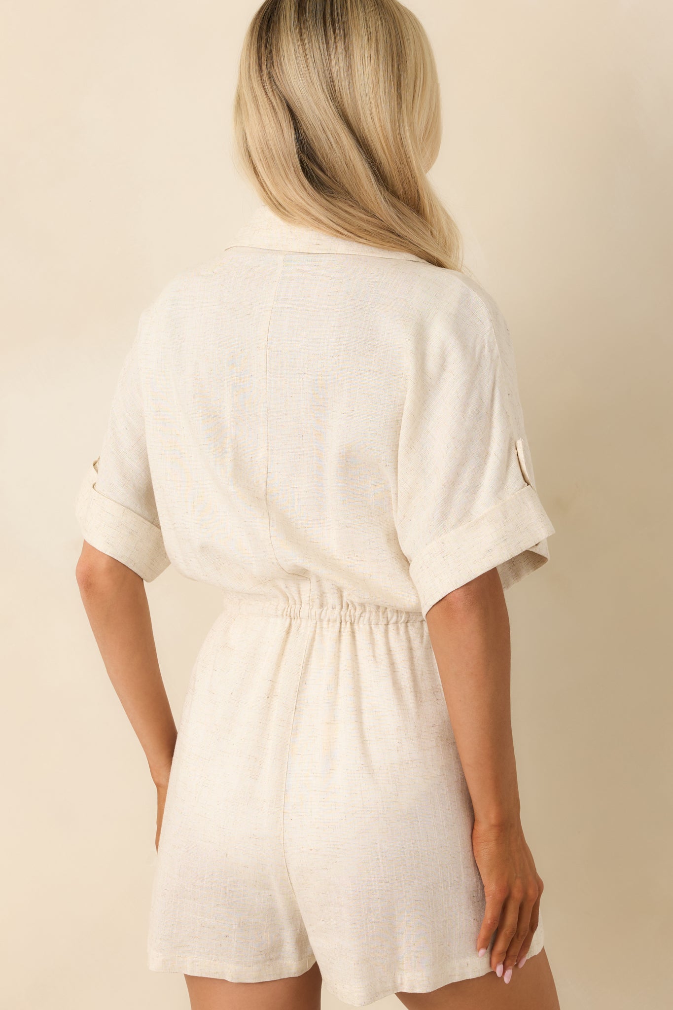 Back view of the beige romper highlighting the straight hem, cuffed sleeves, and smooth linen finish.
