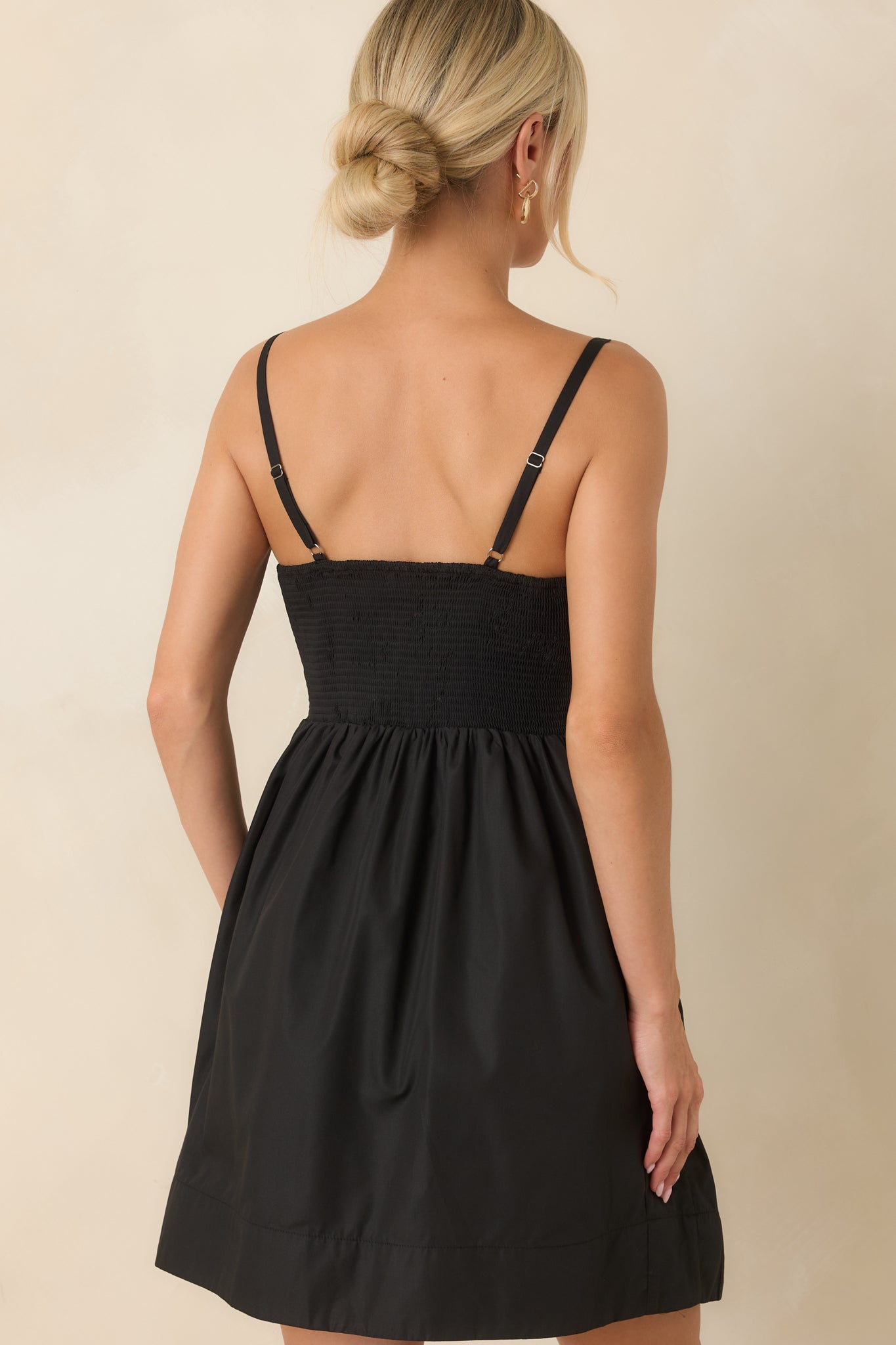 Back view of the black pleated mini dress featuring a stretchy smocked back and adjustable straps.