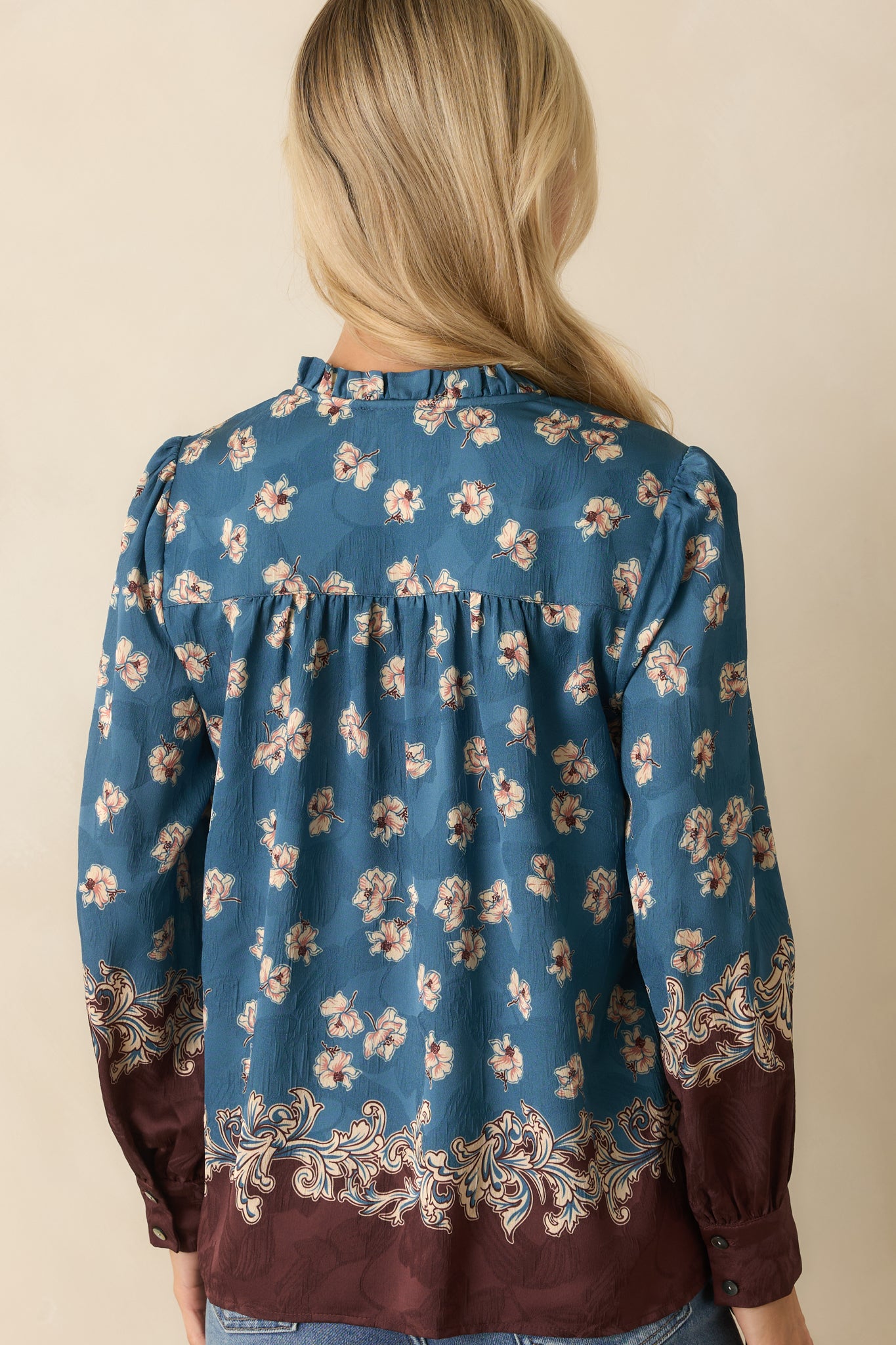 A back view of the blue blouse featuring the floral print fabric, long balloon sleeves, and relaxed fit silhouette.