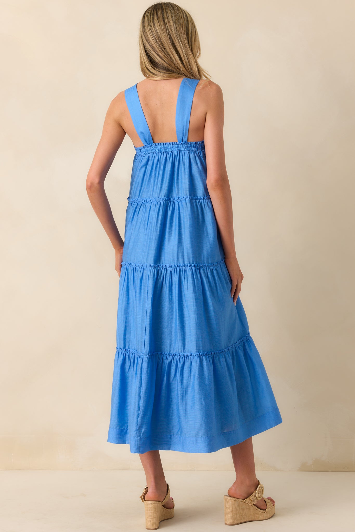 Back view of the blue midi dress showing the relaxed fit, subtle ruffle tiers along the back, and functional pockets integrated into the design.