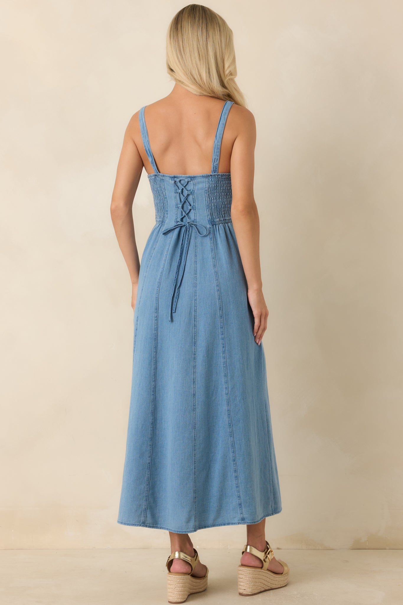 Back view of the cotton denim midi dress featuring a smocked back panel and adjustable lace-up detail.