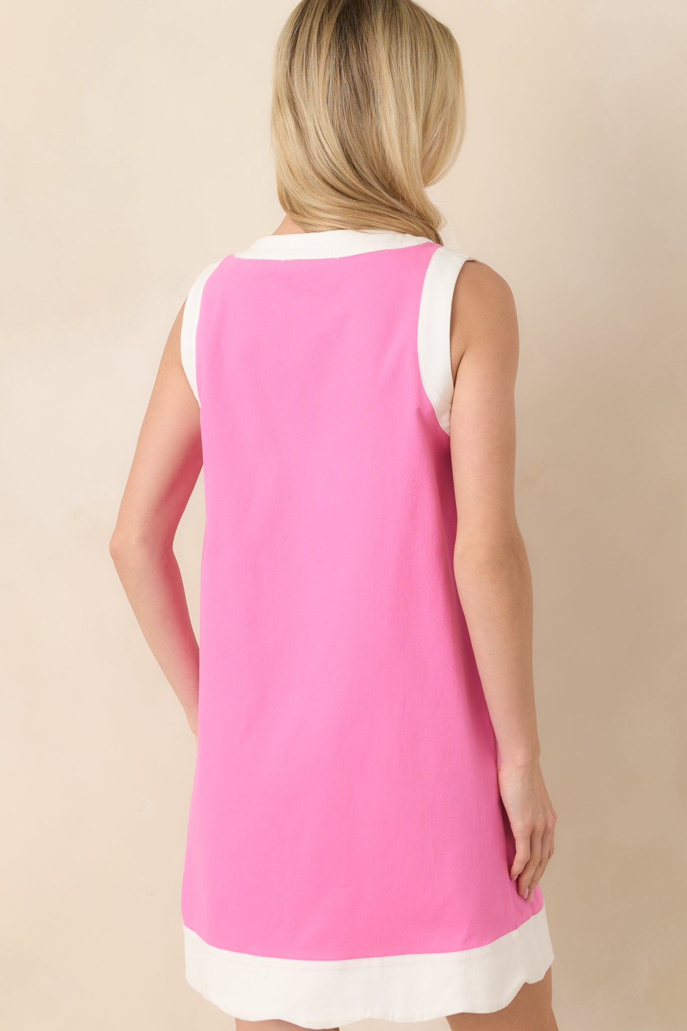 Back view of pink sleeveless cotton mini dress featuring a clean silhouette with contrast trim along the arm openings and hem.