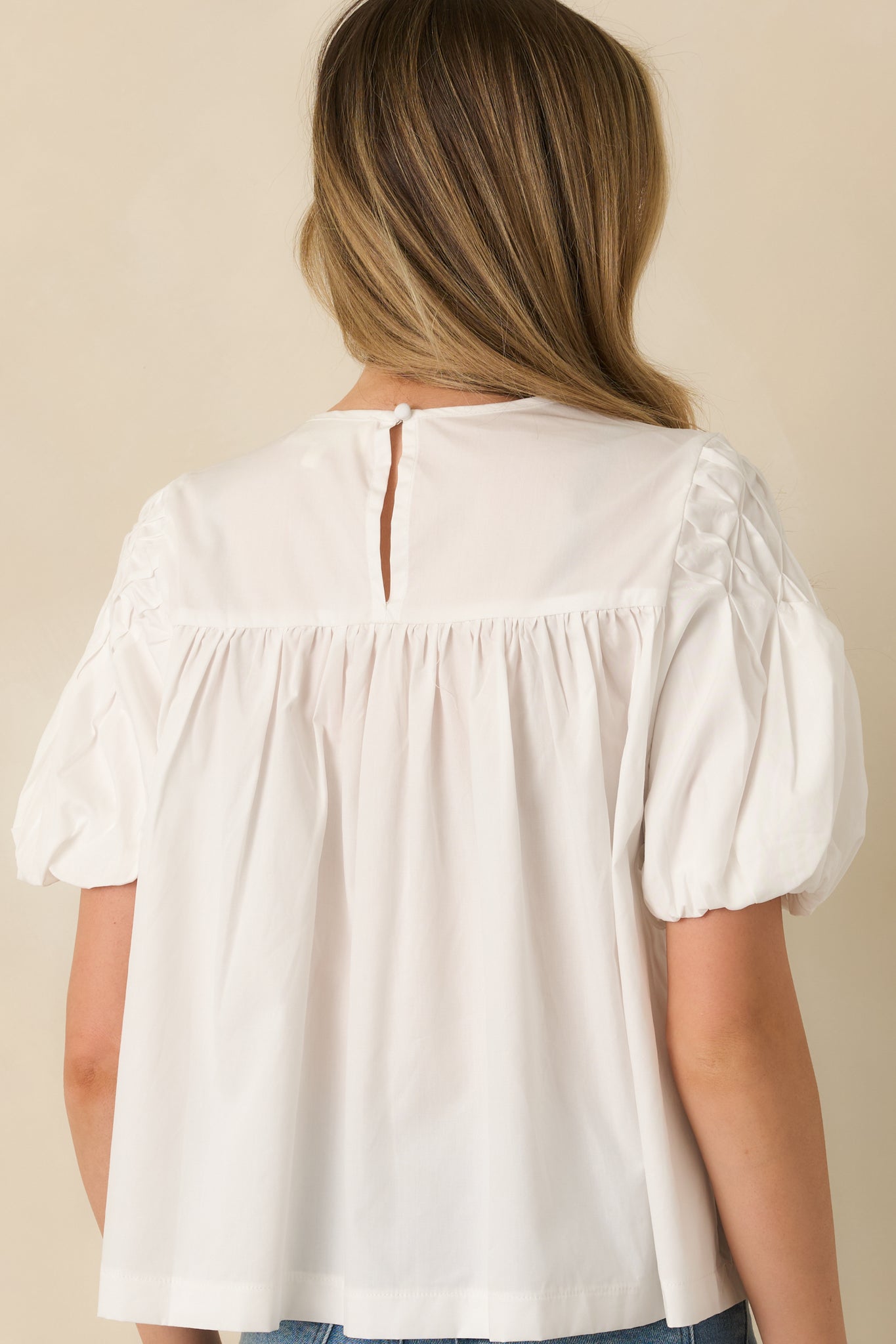 Back view of a white top featuring a back yoke seam and keyhole closure at the neckline.