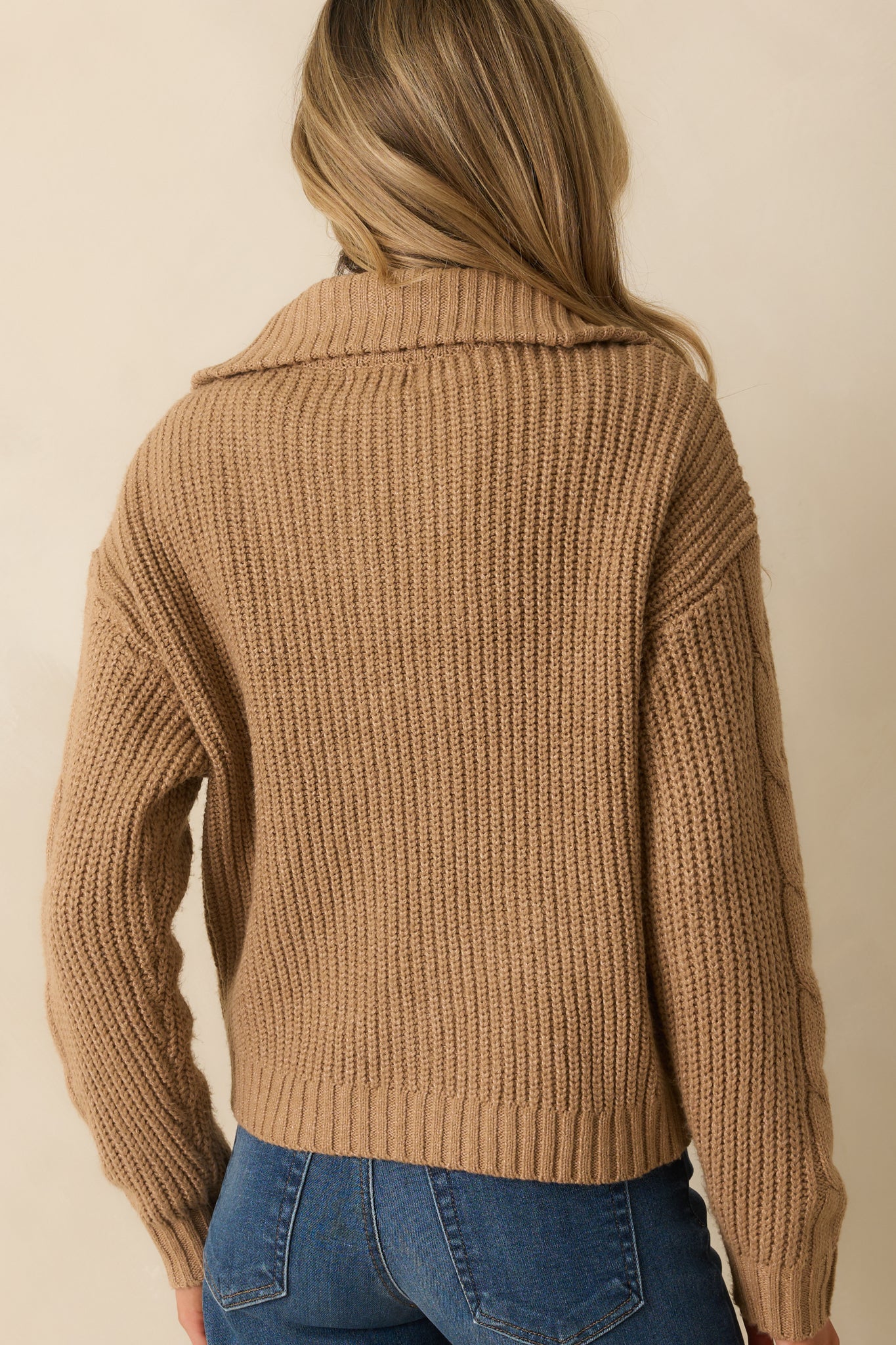 A back view of the camel brown jacket featuring long sleeves, cable knit texture, and ribbed hemline.