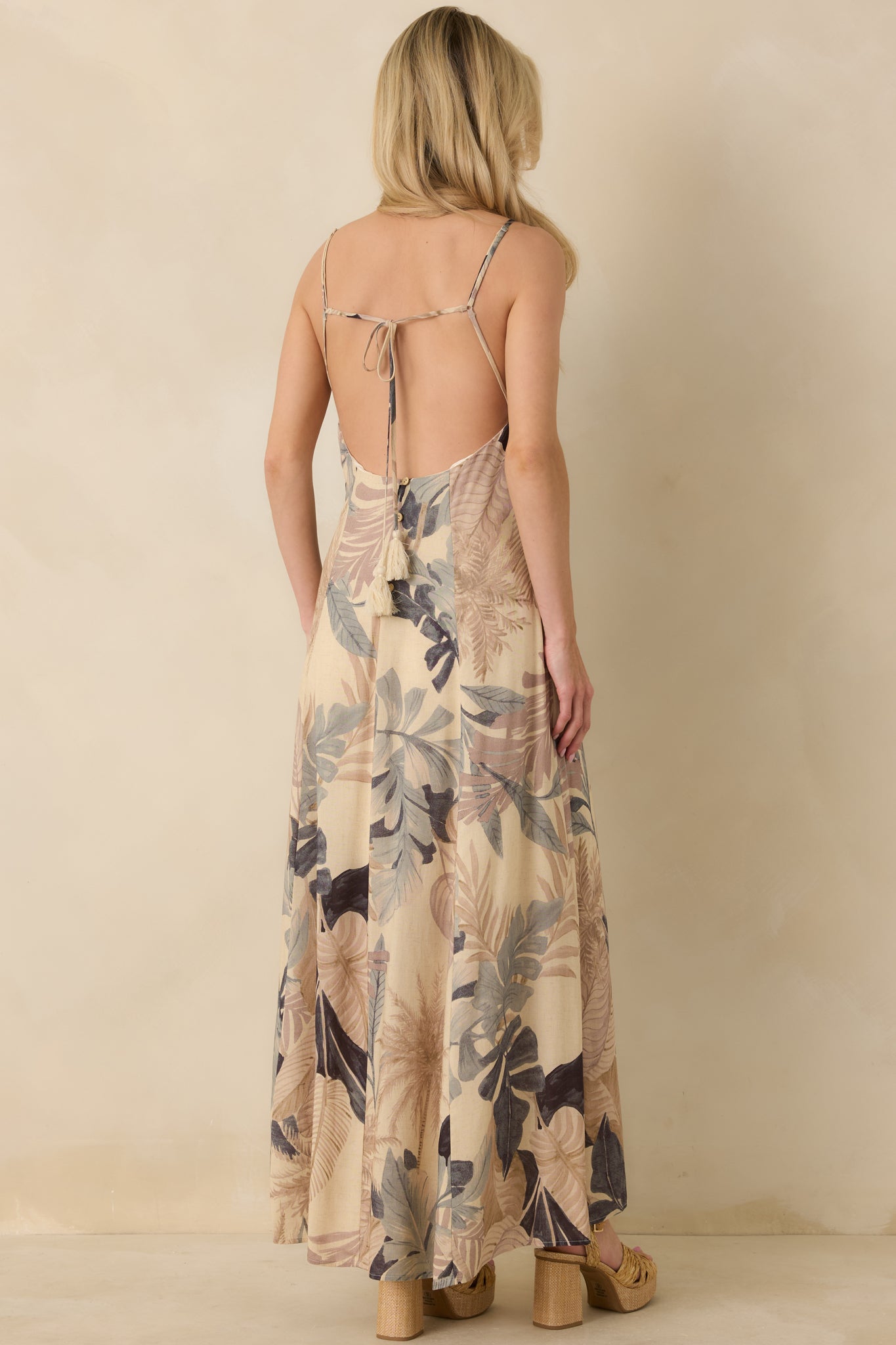 Back view of beige tropical maxi dress featuring open back design and tie-back detail.