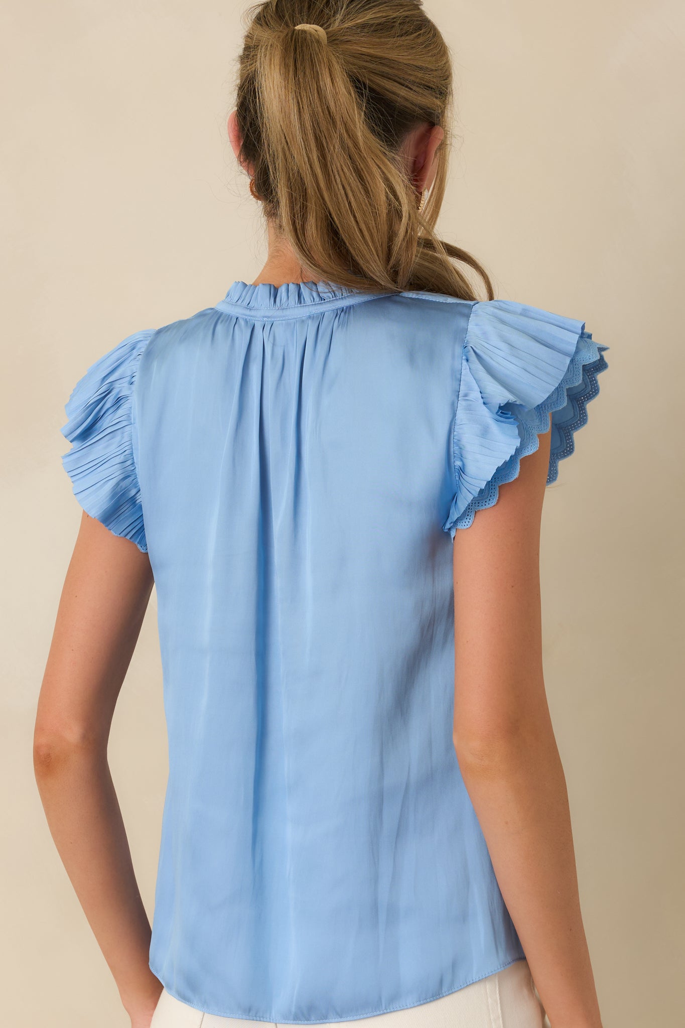 Back view of the blue blouse featuring lightweight semi-sheer fabric, soft drape, and flutter sleeve detail.