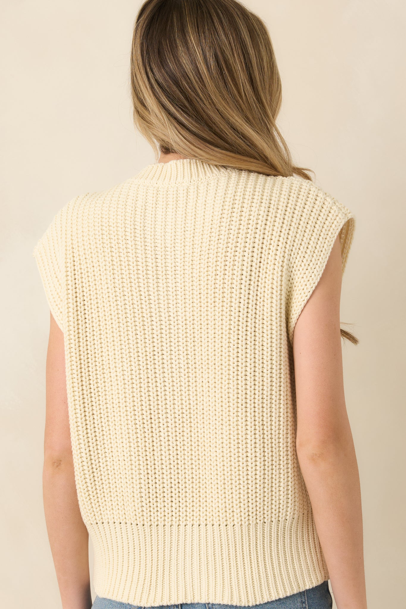 Back view of a sleeveless ivory knit cardigan, highlighting soft textured fabric and clean, structured silhouette.