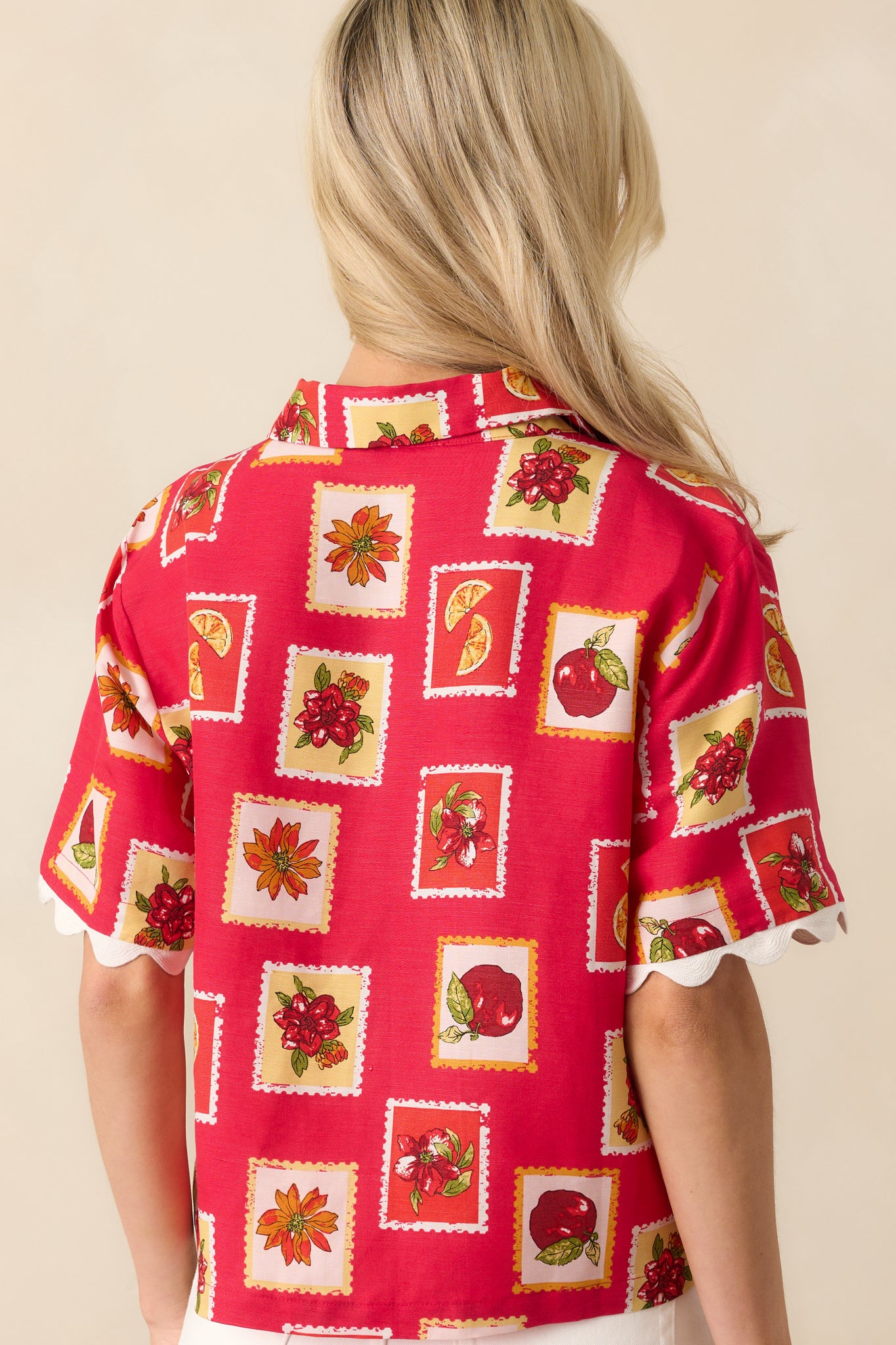 Back view of the red top highlighting the all-over patchwork pattern, short sleeves, and scallop trim at the hem and sleeves.