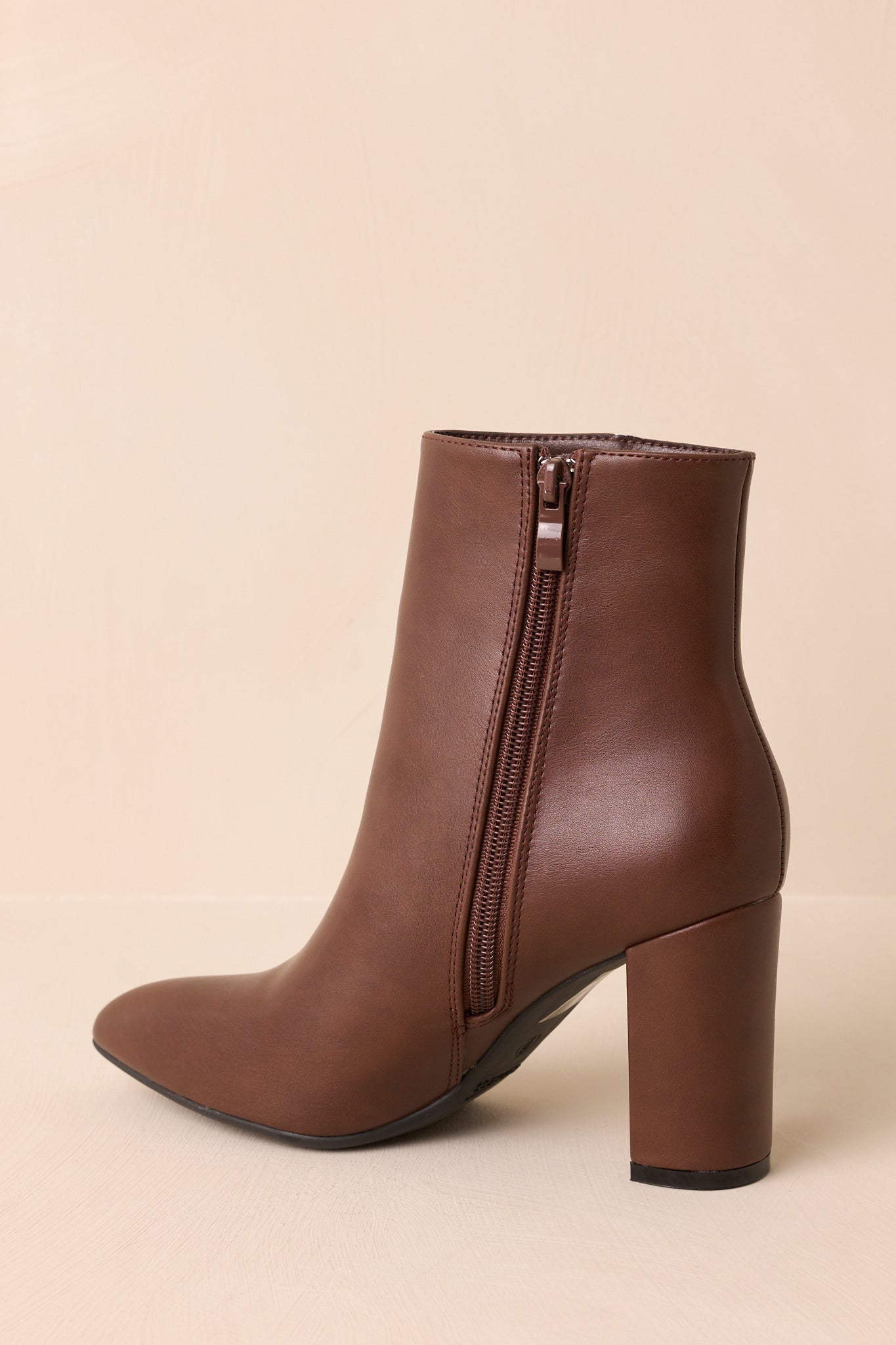 An angled back view of the ankle boots highlighting the brown zipper, block heel, and overall silhouette.