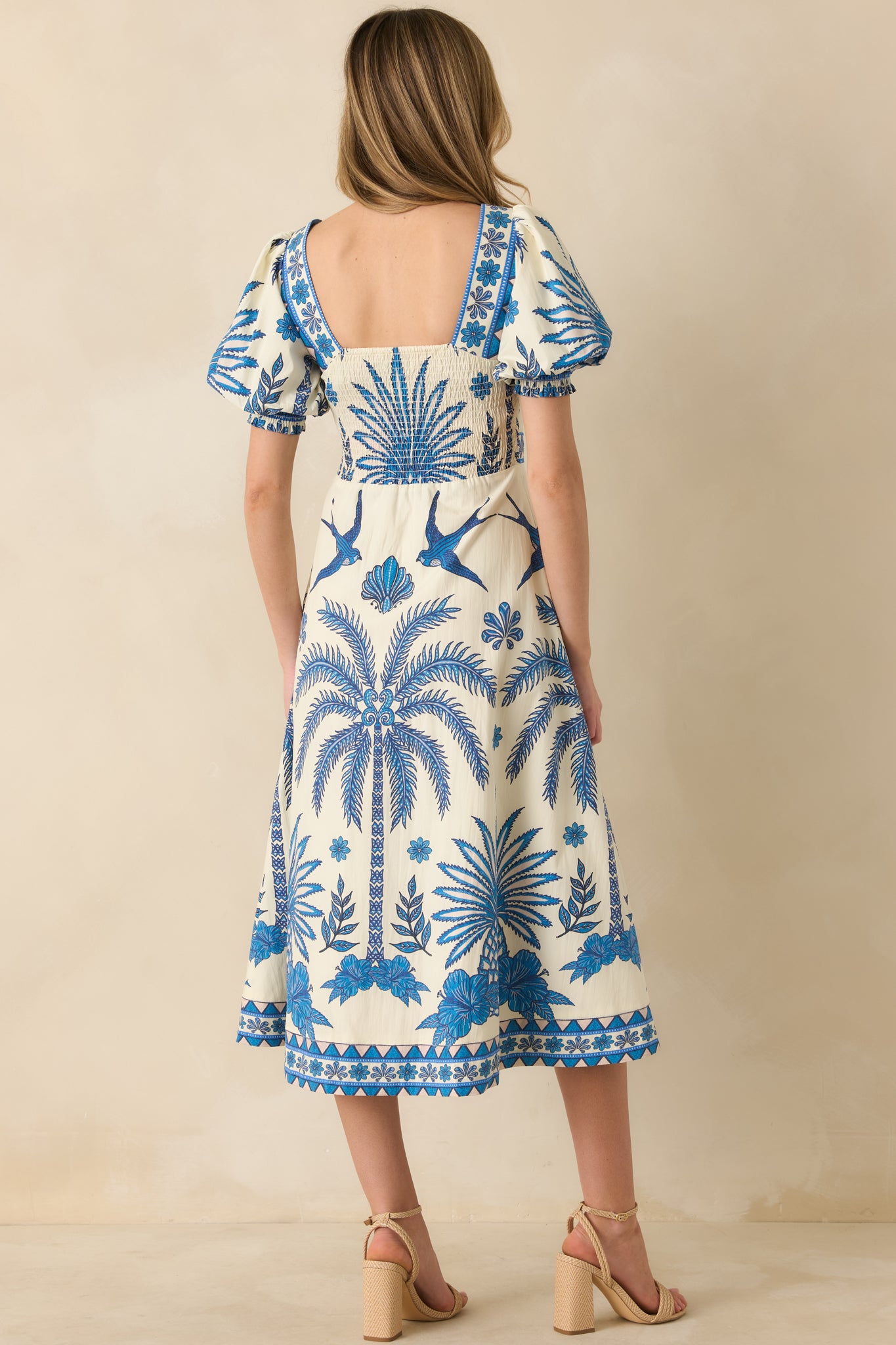 Back view of the blue and ivory midi dress highlighting the smocked back panel and tropical print.