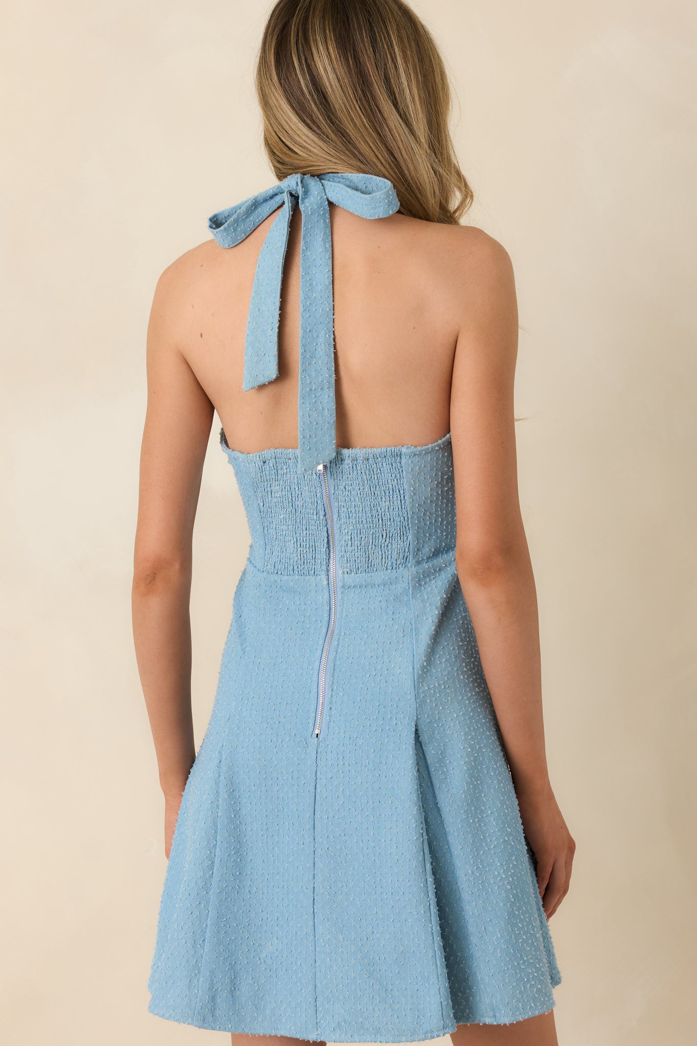 Back view of the blue halter mini dress highlighting the tie-back neckline, smocked panel, and zipper closure.