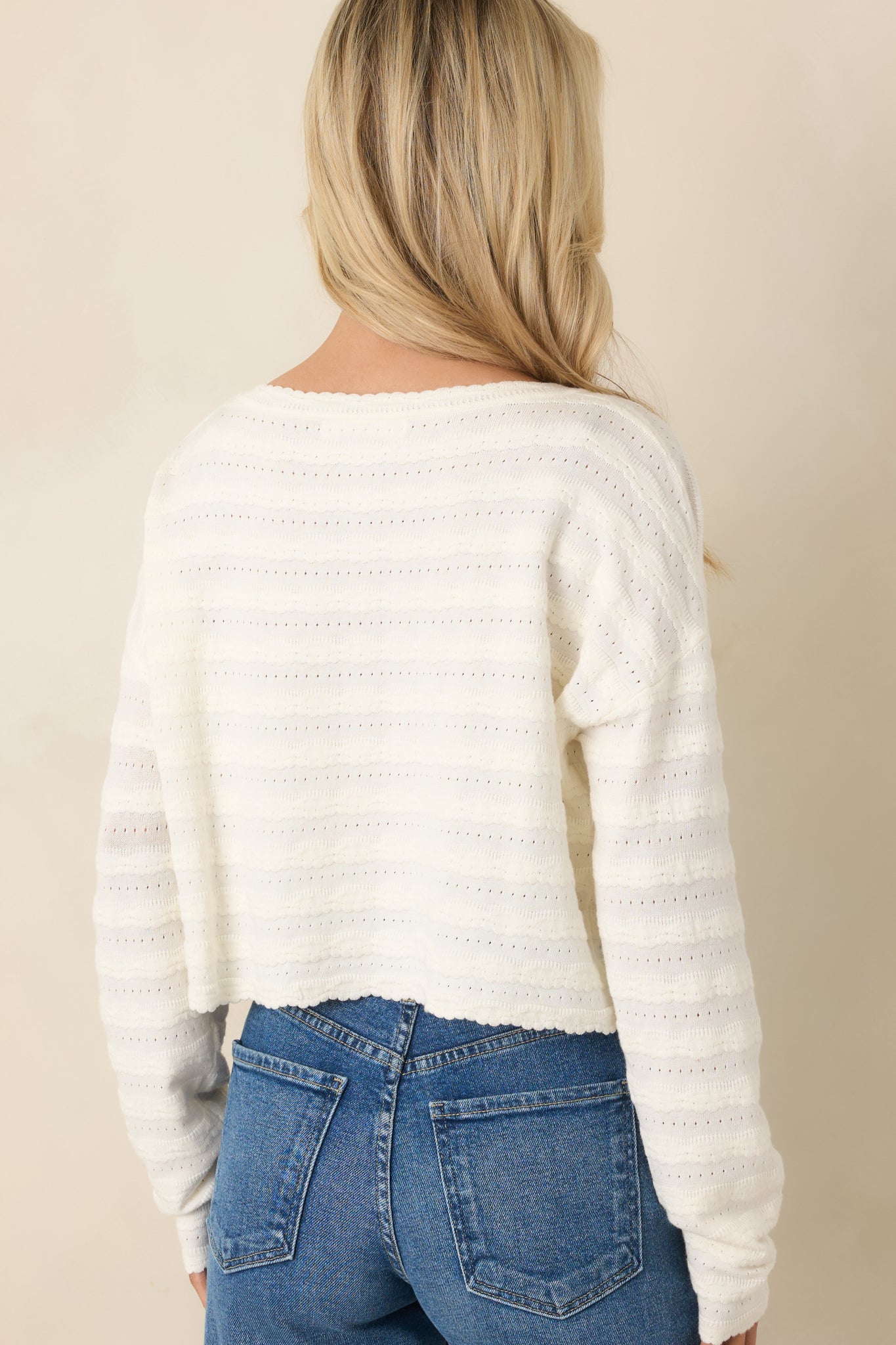 Back view of ivory cardigan sleeve and hem detail showcasing the softly scalloped trim and lightweight knit construction.