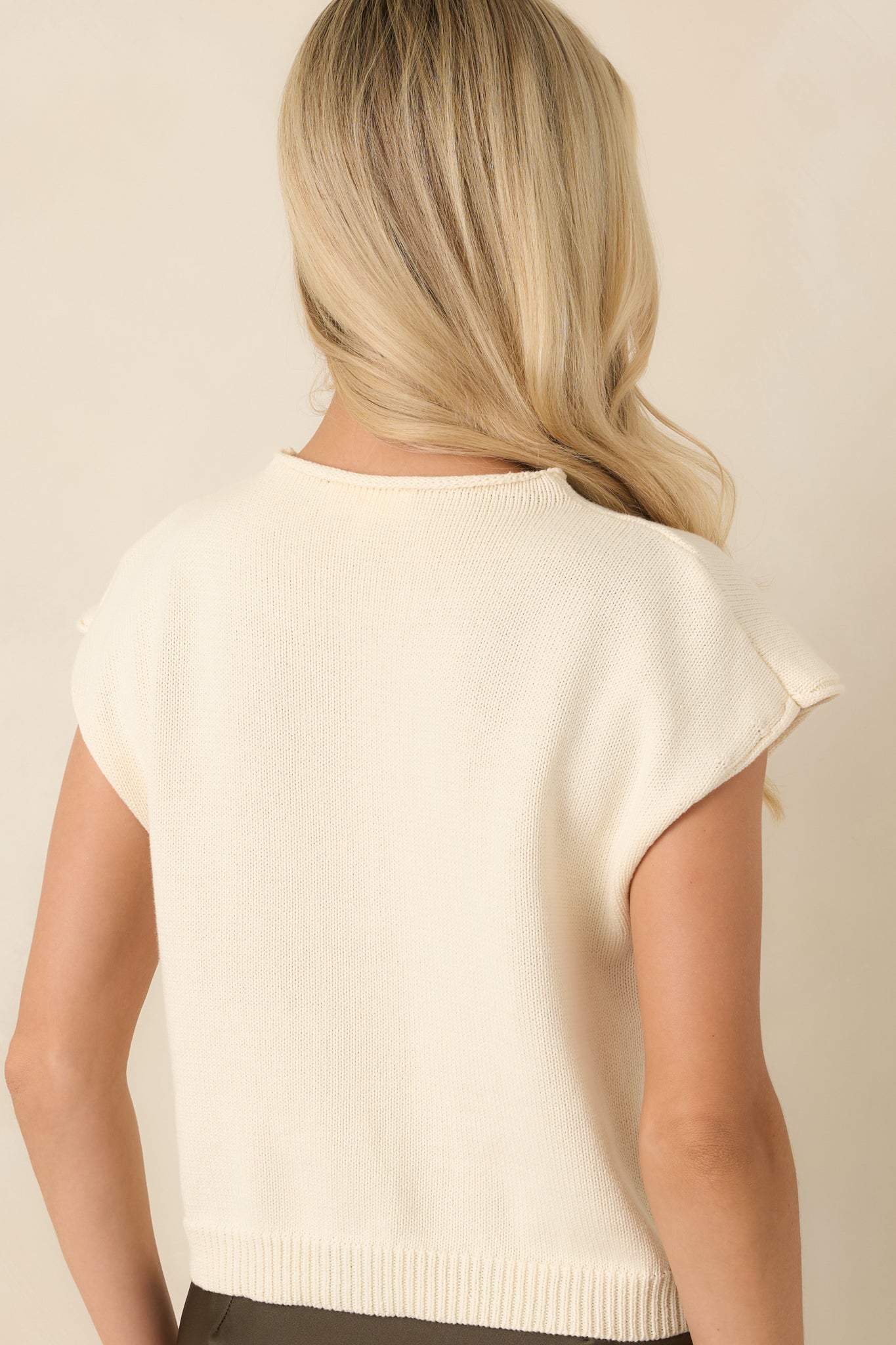 Back view of the ivory knit top featuring a sleeveless silhouette and ribbed hem finish.