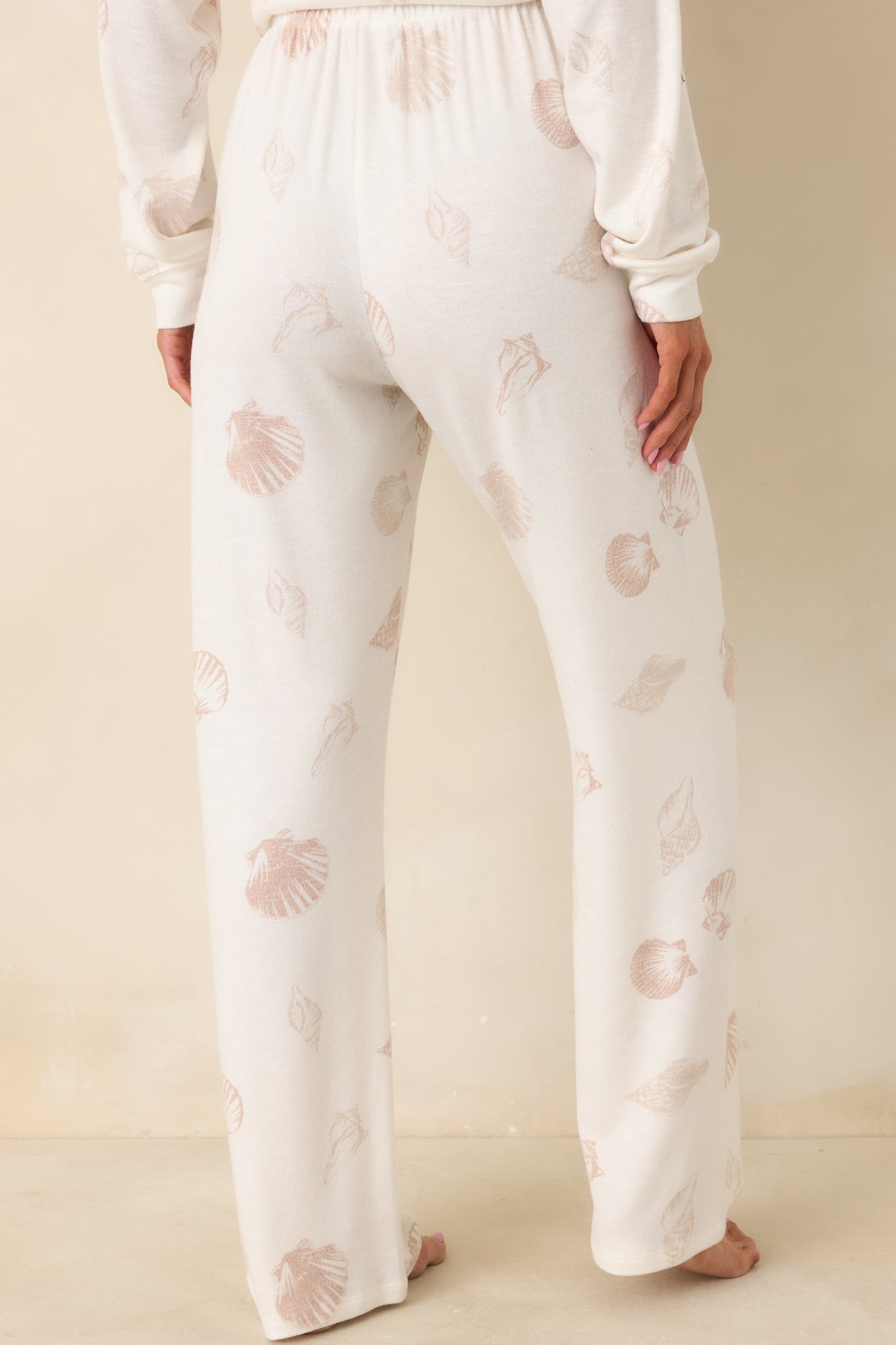 Back view of ivory pajama pants featuring relaxed wide-leg silhouette and allover neutral seashell print in breathable knit fabric.
