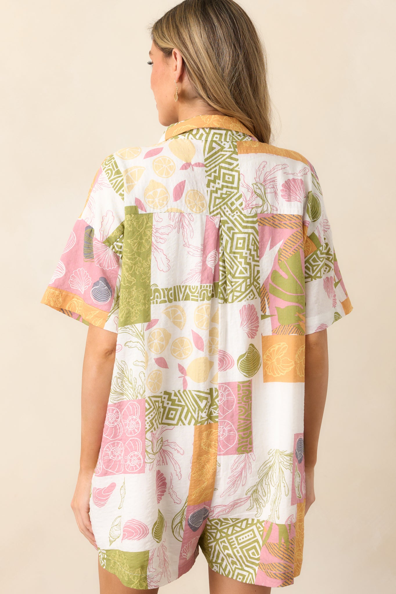 The back of the ivory romper, displaying the continuation of the tropical patchwork design and the structured fit of the short-sleeve silhouette.