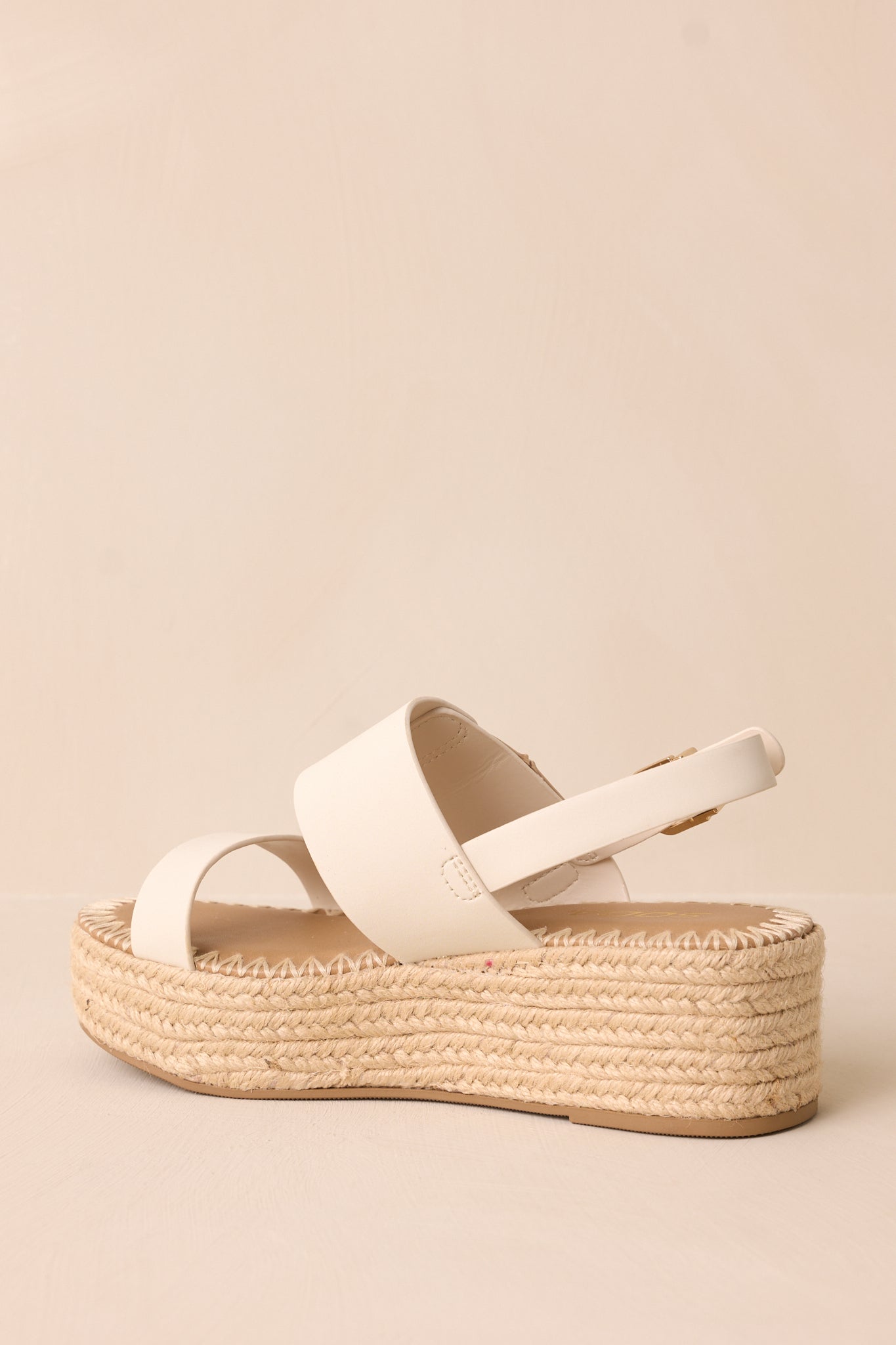 A back view of the ivory sandals, featuring the ankle strap with a gold buckle and the woven wedge heel for a polished yet natural look.