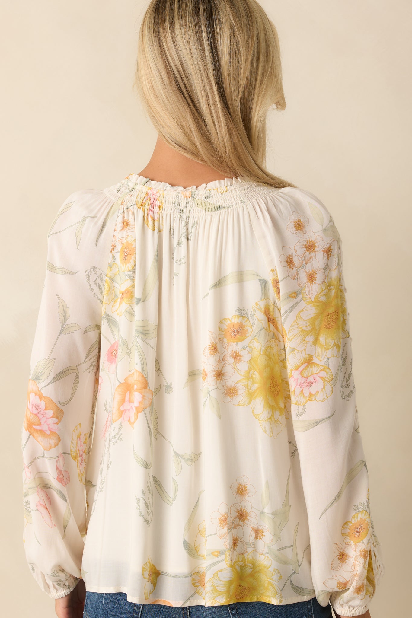 A back view of the ivory top showing long sleeves, elastic cuffs, and floral print across the back.