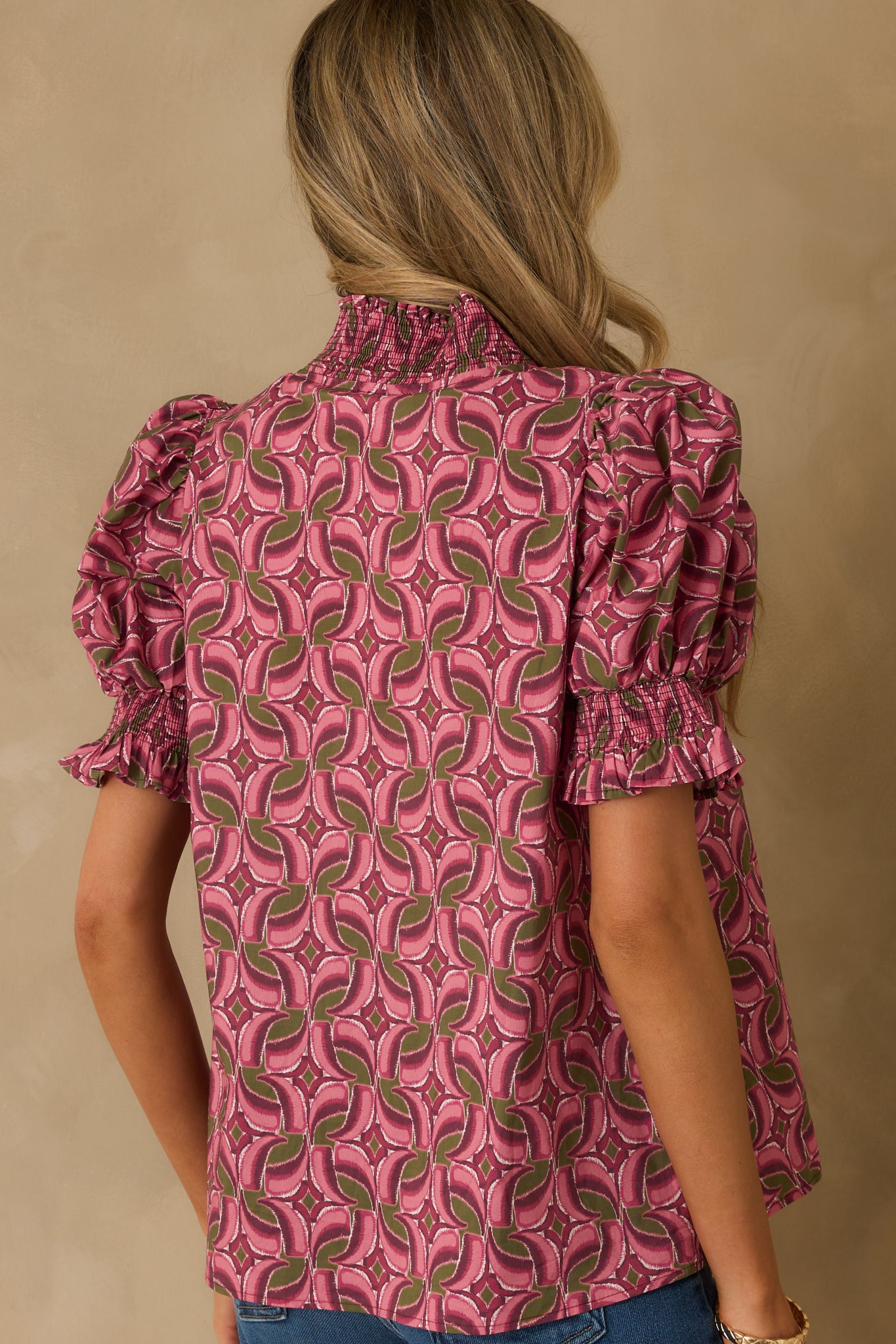 Back view of the top showing the light mauve fabric, short puff sleeves, and scoop hem from behind.