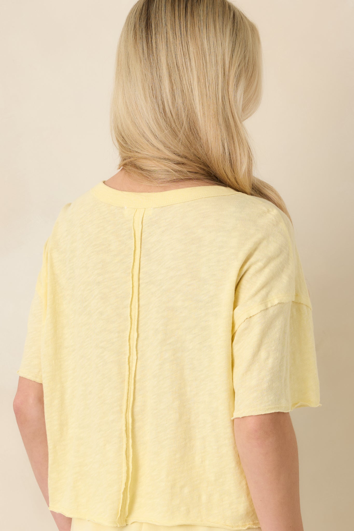Back view of the light yellow relaxed-fit tee displaying short sleeves, slightly cropped length, and clean cotton drape.
