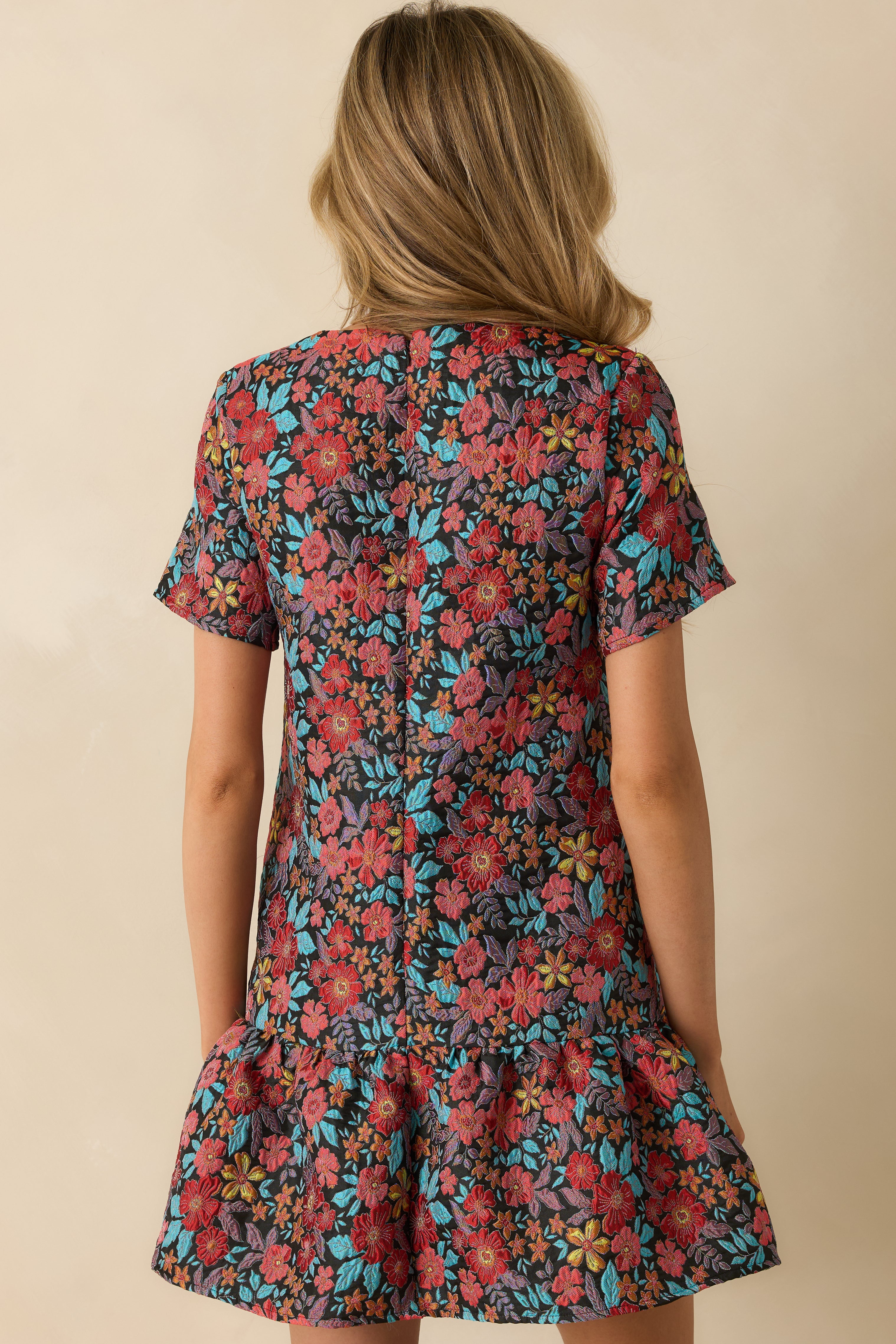 Back view of the mini dress displaying the short sleeves, drop waist, and ruffled hem from behind.