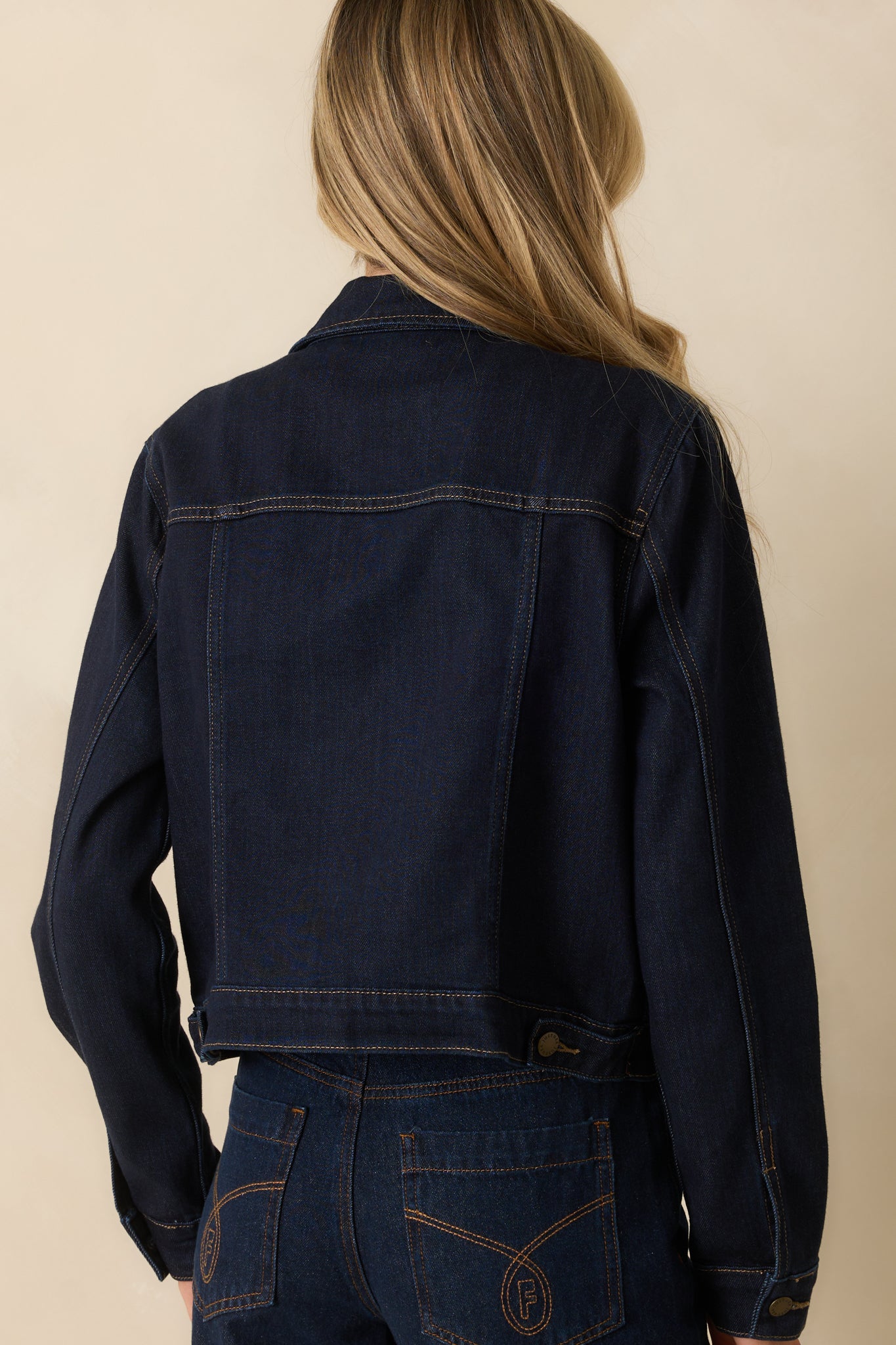 A back view of dark wash denim jacket showing structured seams and contrast stitching.