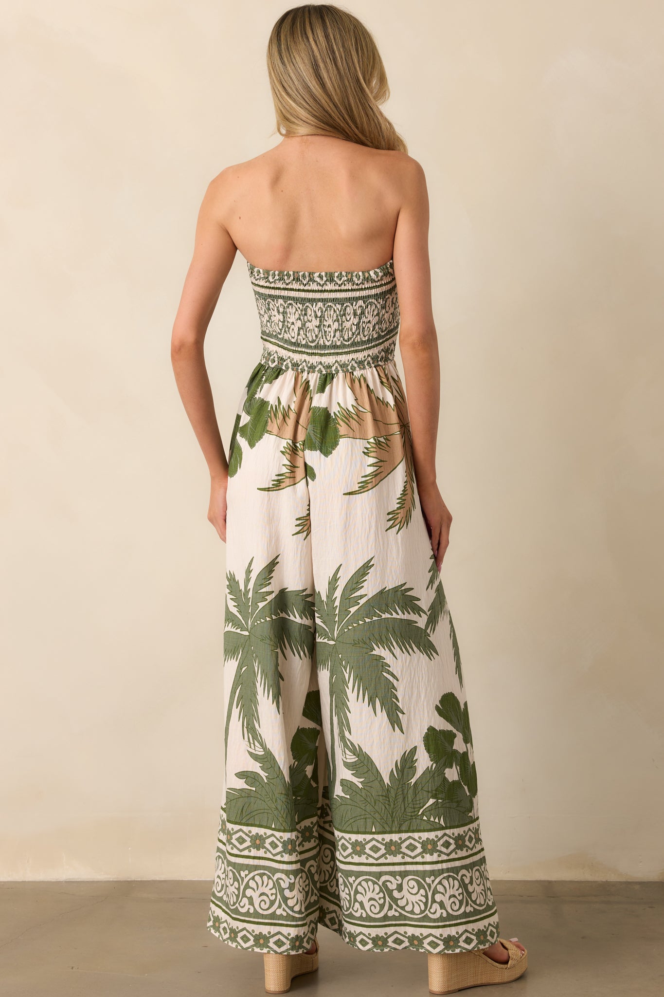 Back view of the jumpsuit featuring the smocked back panel and continuation of the green and tan tropical print.